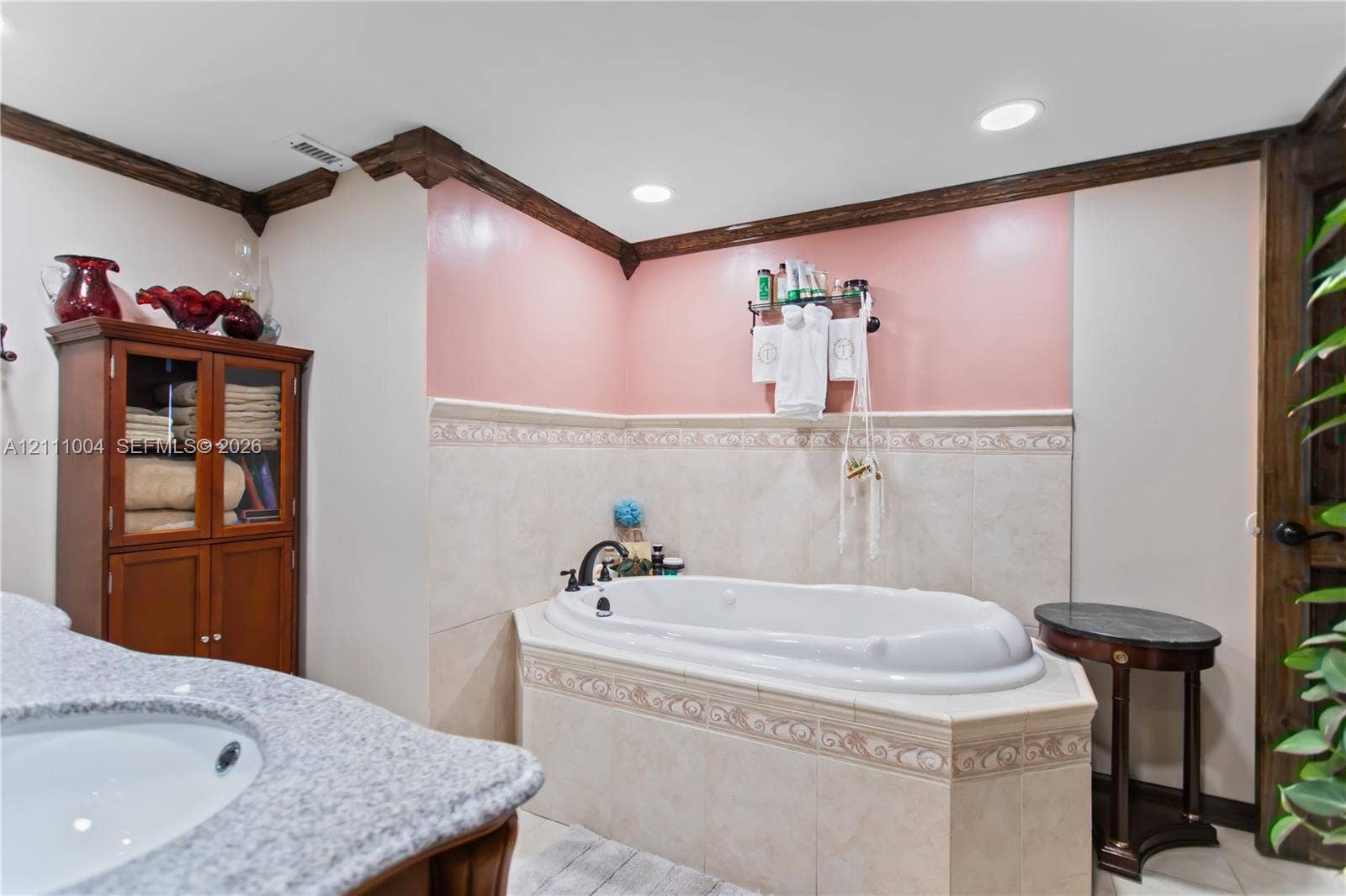 Bathroom featuring a jetted soaking tub with tiled surround, built-in wooden cabinetry, stone-finish countertop with integrated sink, crown molding, and recessed lighting
