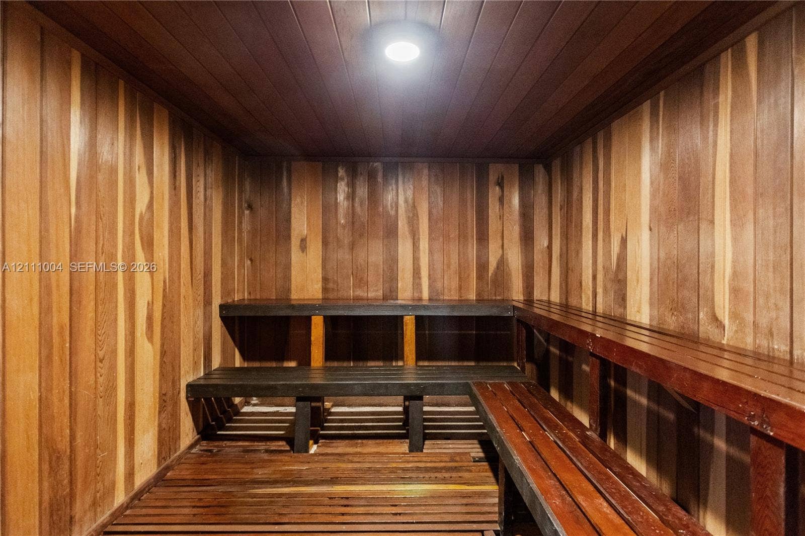 Sauna featuring wood-paneled walls, tongue-and-groove ceiling, multi-level slatted benches, and recessed lighting