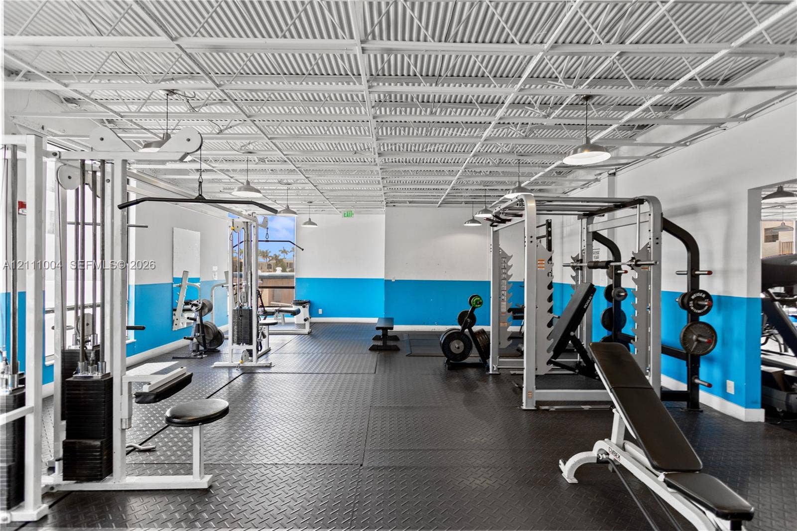 Fitness facility featuring industrial-style exposed metal ceiling grid, durable rubberized flooring, and recessed pendant lighting