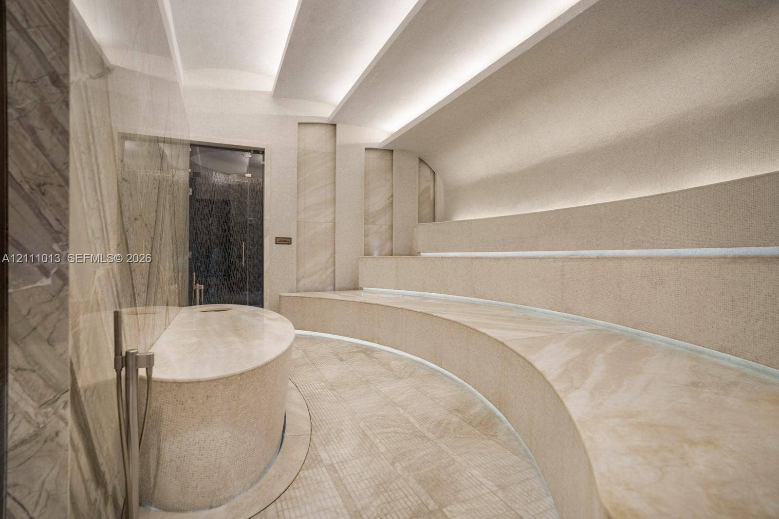 Steam room featuring integrated stone bench seating, expansive stone slab flooring, built-in cove lighting, and polished stone wall accents