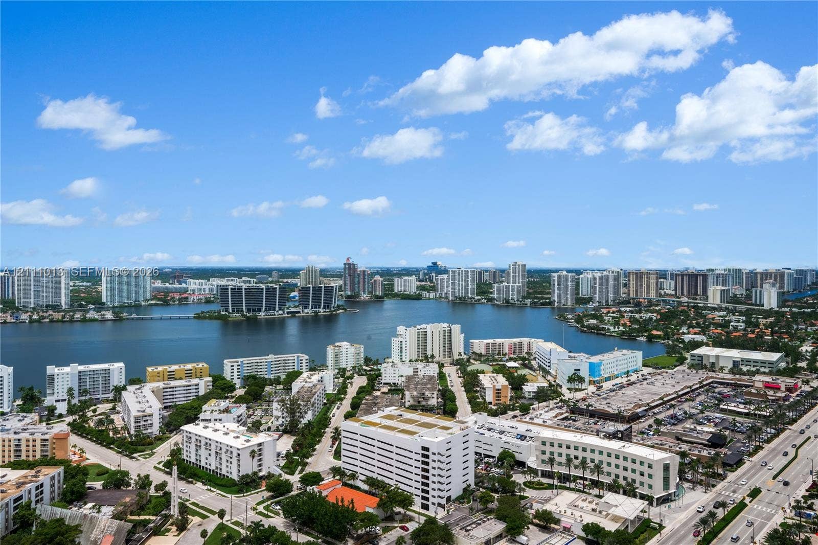 Aerial perspective of a coastal urban landscape featuring multiple high-rise structures, an expansive inland waterway, dense foliage, and established roadway infrastructure