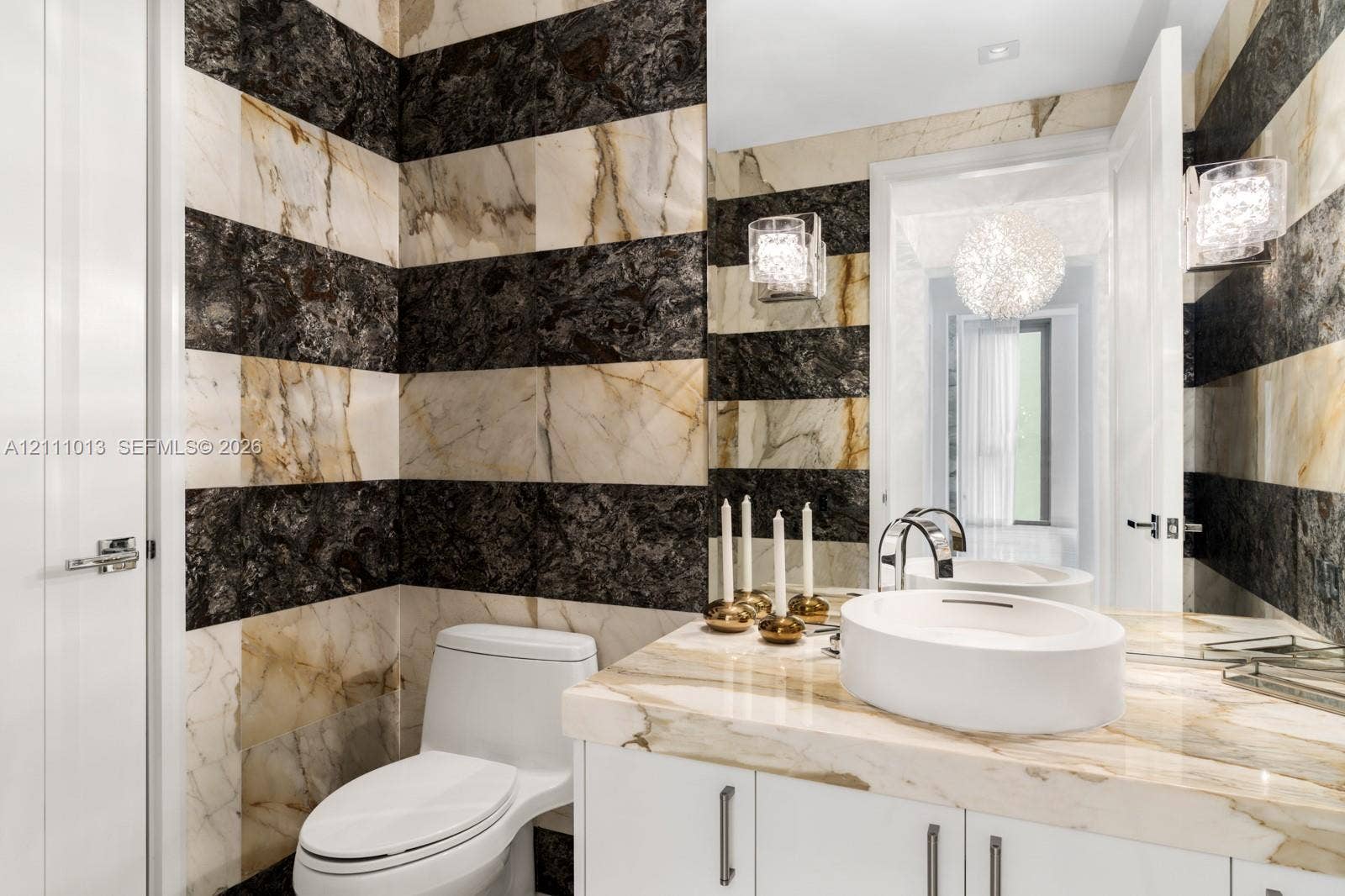 Floor-to-ceiling high-contrast natural stone wall tile, custom vanity with a matching stone countertop, vessel sink, chrome high-arc faucet, and integrated wall-mounted lighting