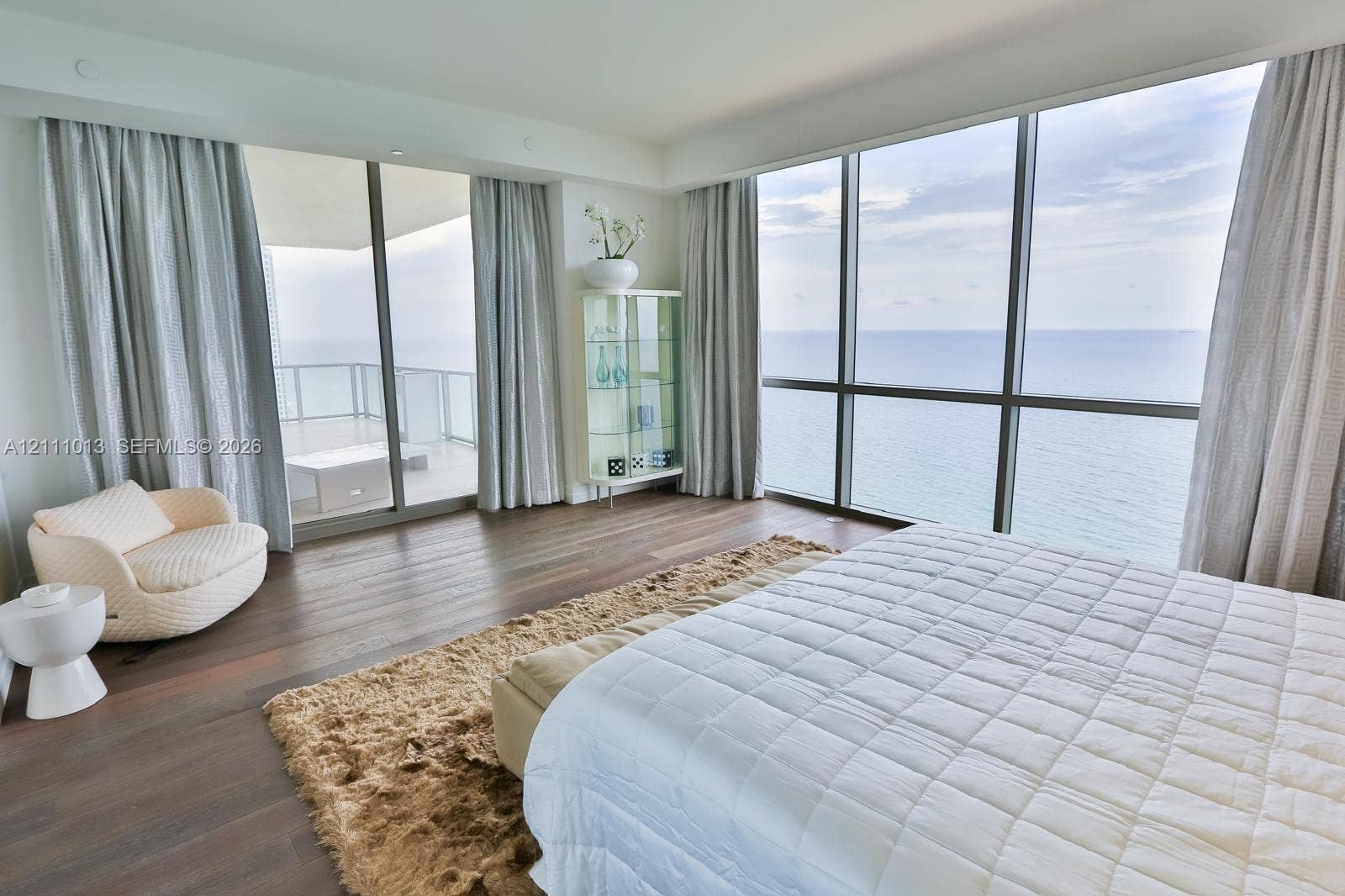 Floor-to-ceiling glass walls, wood-finish flooring, and a private balcony featuring a glass railing