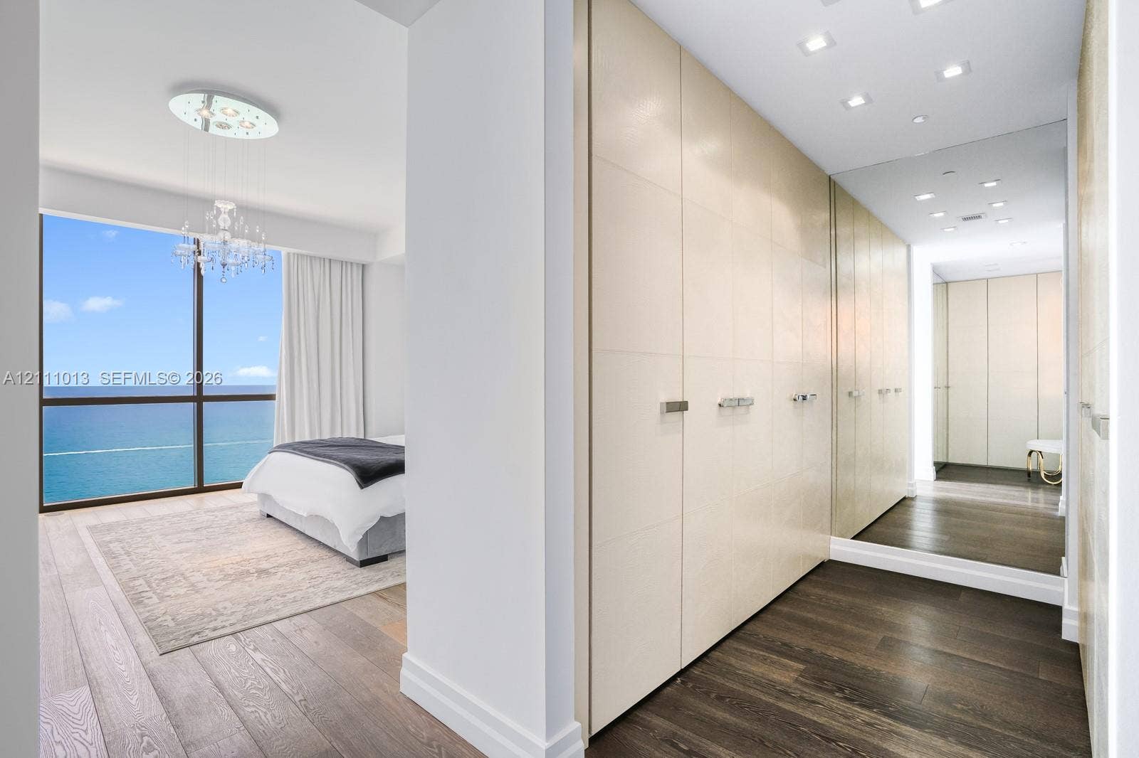 Floor-to-ceiling windows featuring ocean panoramas, built-in floor-to-ceiling cabinetry with metallic hardware, recessed ceiling lighting, and wood-finish flooring
