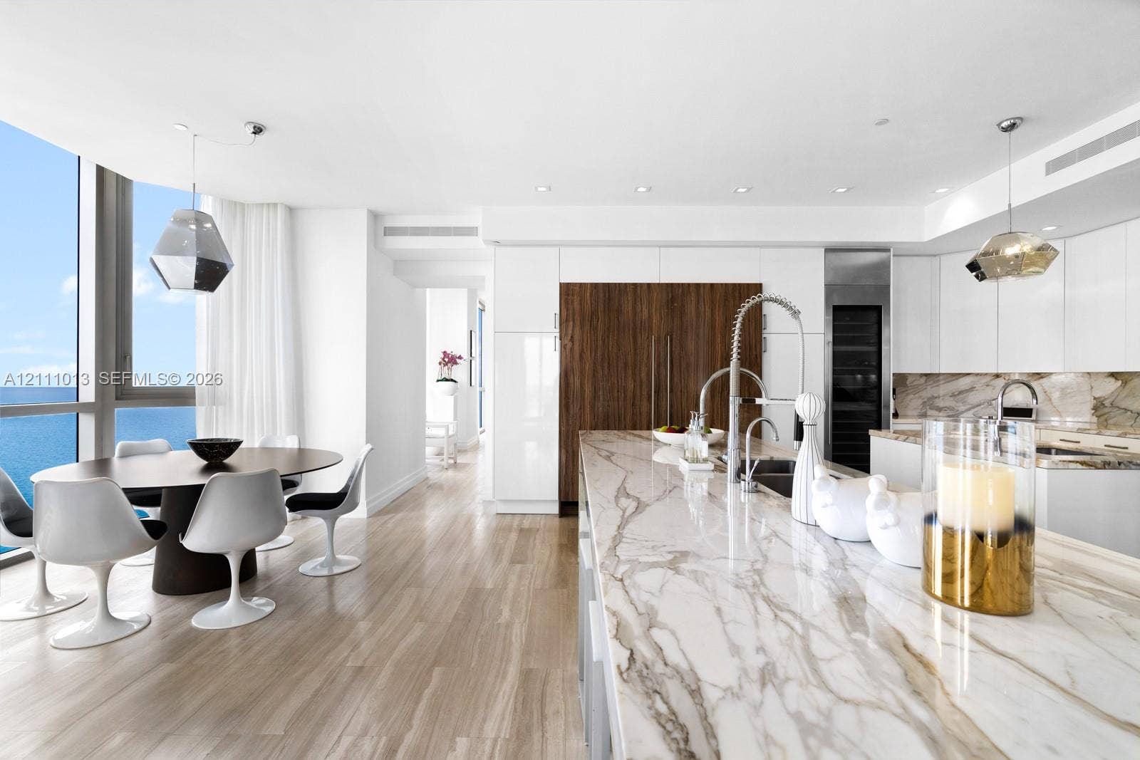 Contemporary kitchen featuring a large stone island with an integrated sink, high-gloss cabinetry, wood-finish flooring, and floor-to-ceiling windows