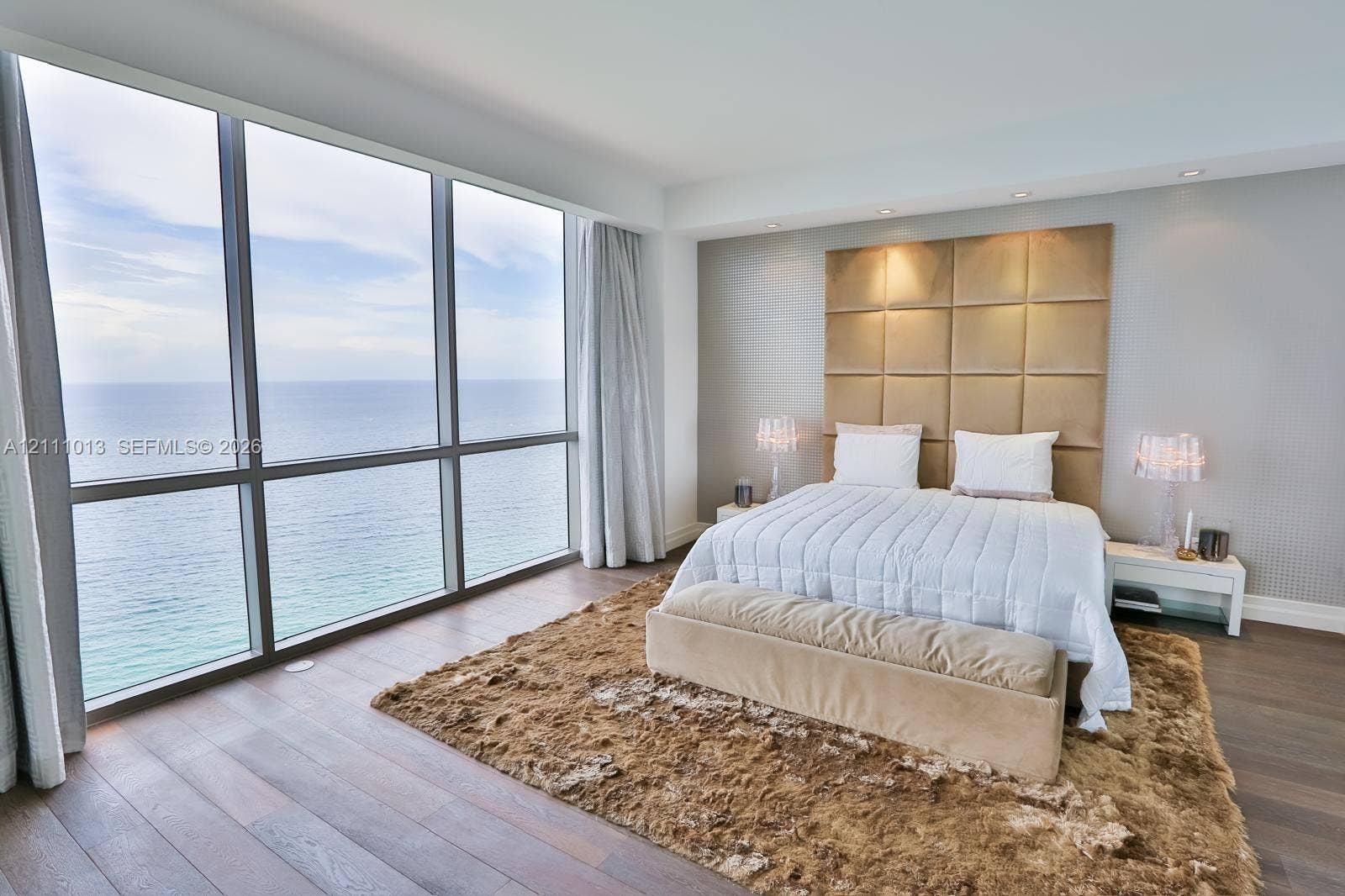 Floor-to-ceiling windows featuring ocean scenery, wood-finish flooring, and a floor-to-ceiling upholstered grid headboard