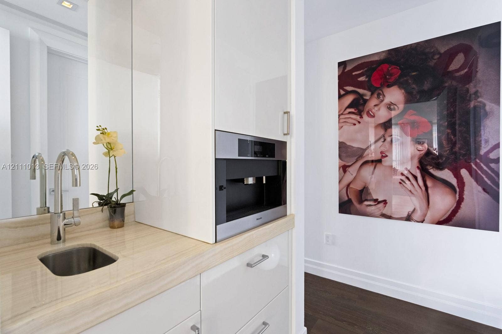 Built-in stainless steel coffee system, high-gloss white cabinetry, polished stone countertop with an integrated basin, and polished chrome faucet