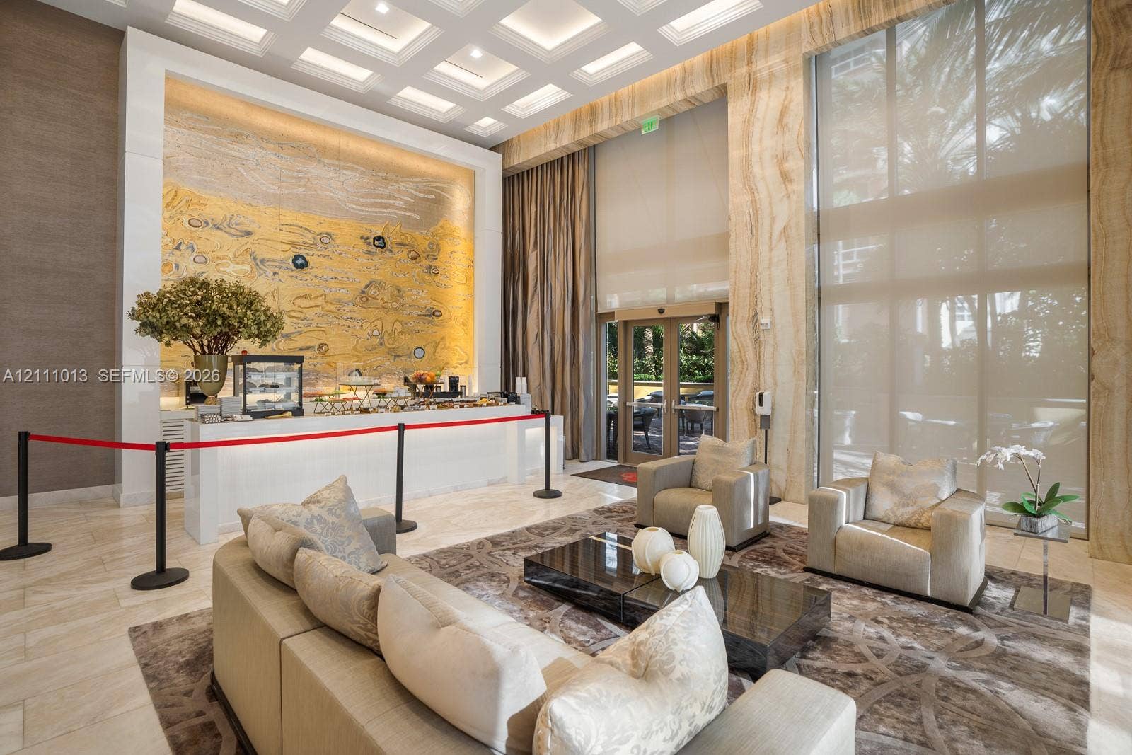 Lobby featuring high ceilings with integrated coffered lighting, stone-clad walls, floor-to-ceiling windows, and a decorative gold-toned tile mosaic accent wall