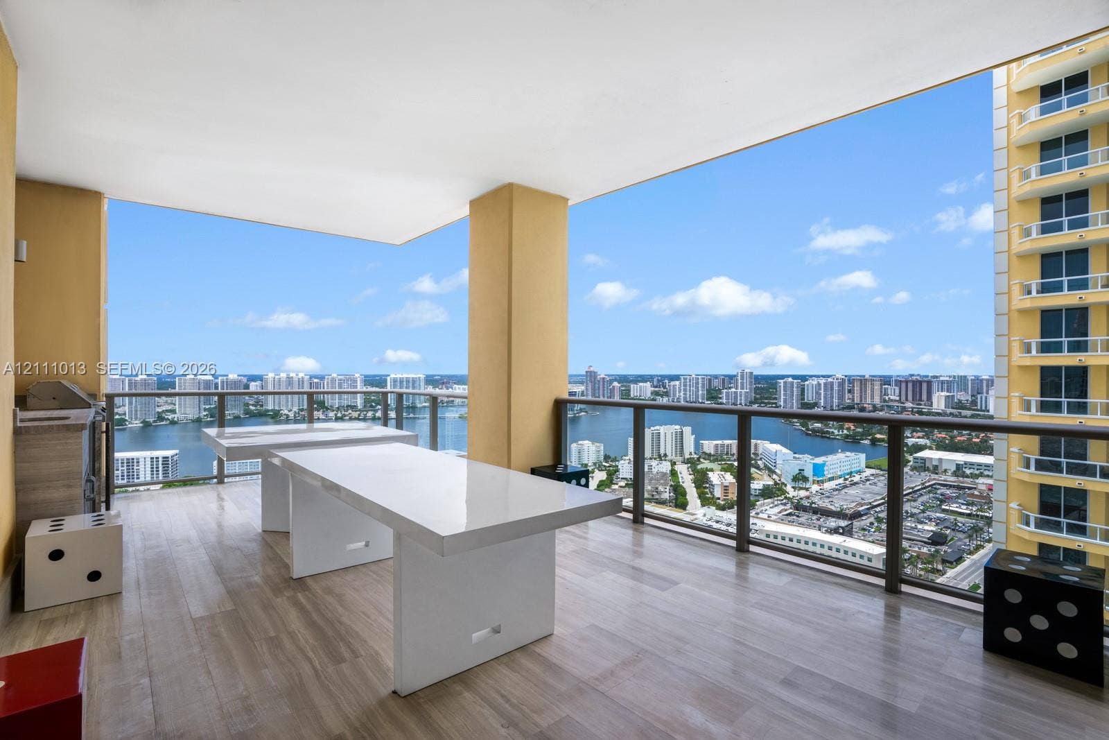 Covered balcony featuring wood-finish flooring, built-in outdoor kitchen station, and a metal-framed glass railing system