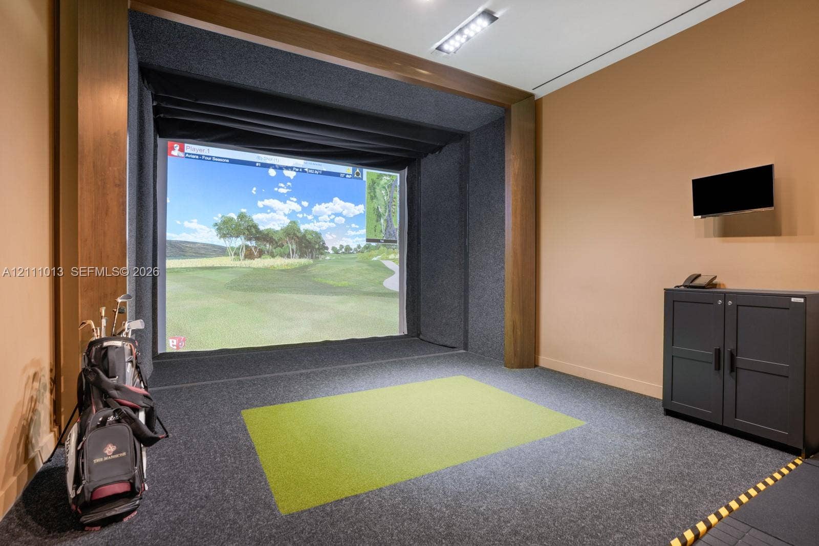 Indoor golf simulator room featuring custom wood-trimmed enclosure, sound-dampening wall panels, integrated ceiling lighting, and built-in cabinetry
