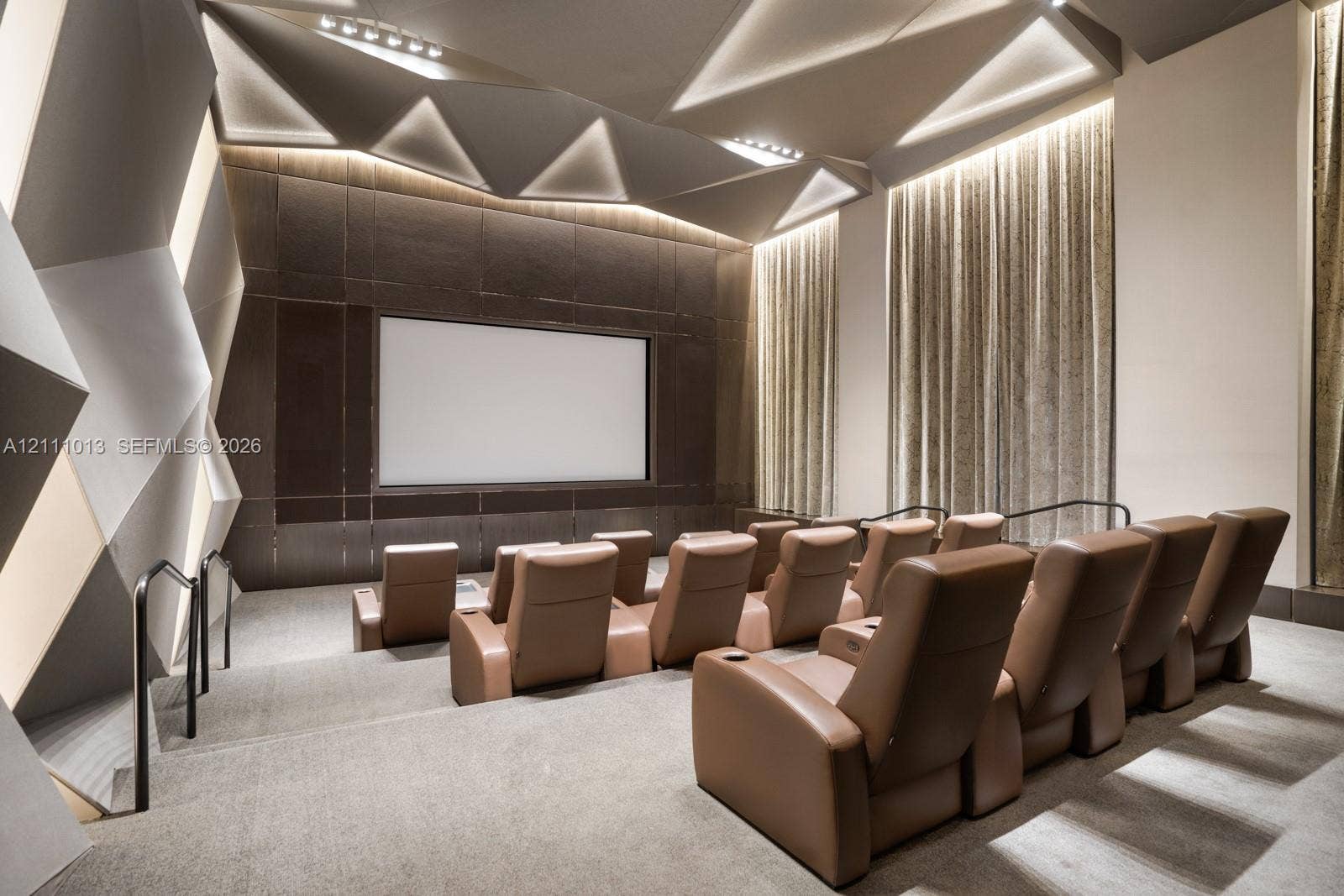 Custom tiered seating area featuring geometric wall paneling, integrated cove lighting, recessed ceiling architecture, and a dedicated projection screen wall