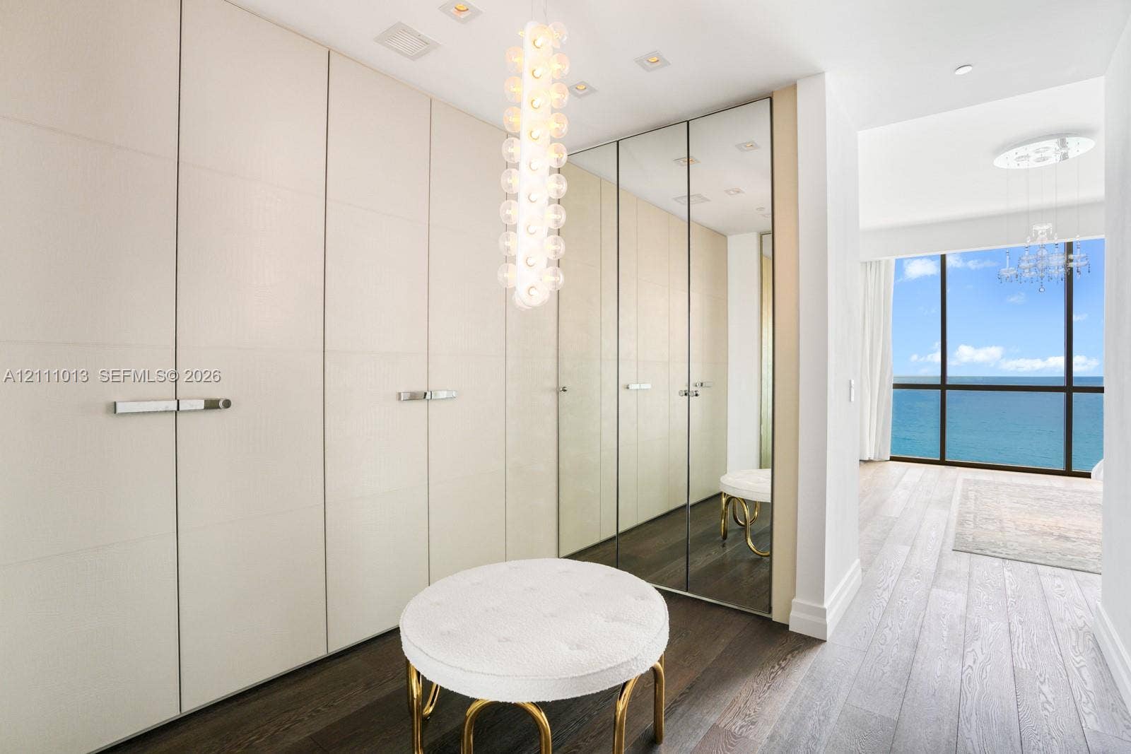 Floor-to-ceiling built-in cabinetry with integrated hardware, mirrored closet doors, wood-finish flooring, custom pendant lighting, and floor-to-ceiling windows featuring an ocean horizon