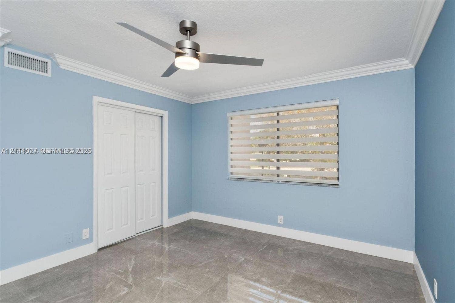 Large-format stone-finish tile flooring, matte metallic ceiling fan with integrated lighting, crown molding, and dual-panel closet doors