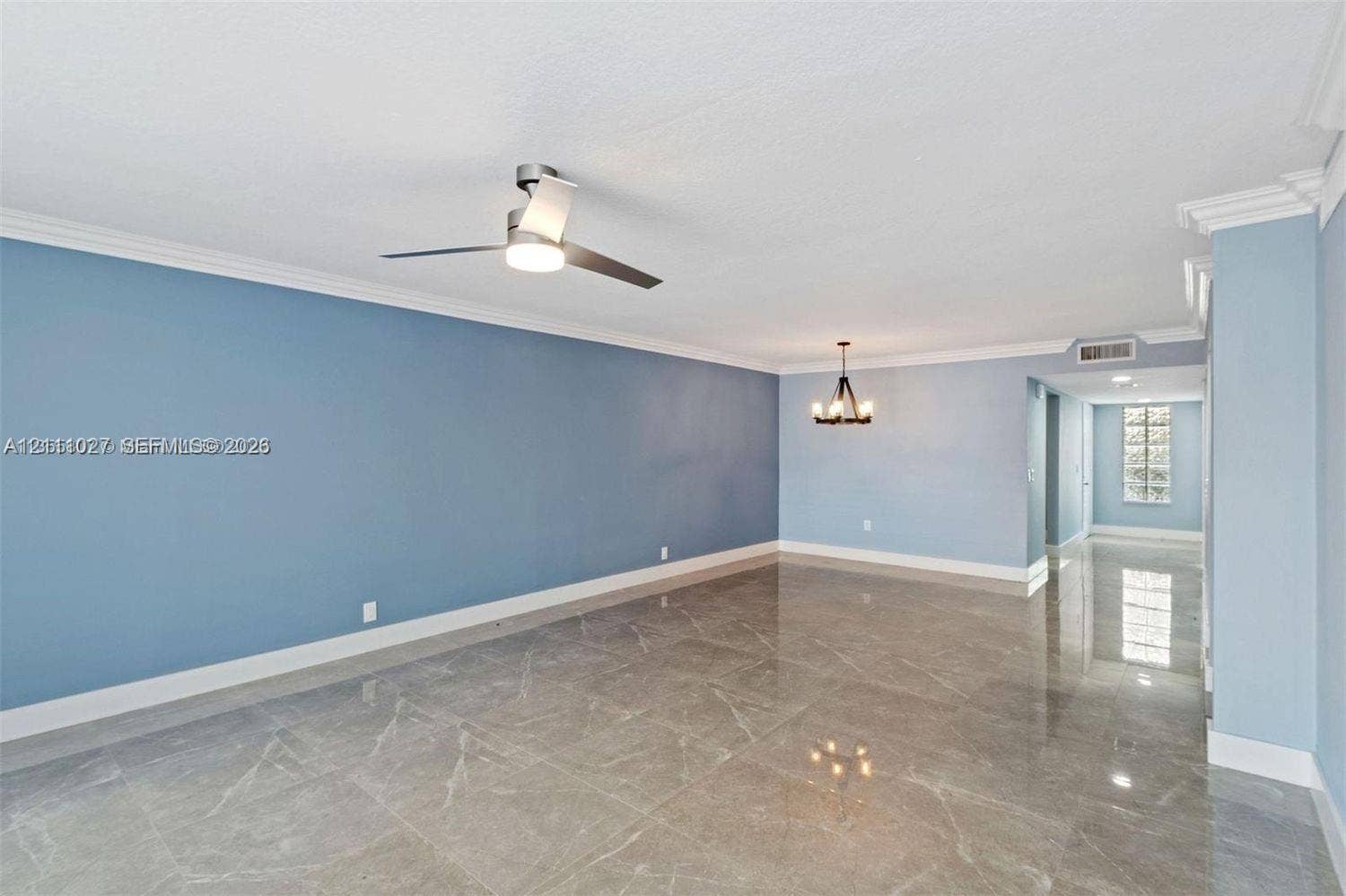 Large-format polished stone flooring, crown molding, modern three-blade ceiling fan with integrated light, and decorative multi-light chandelier