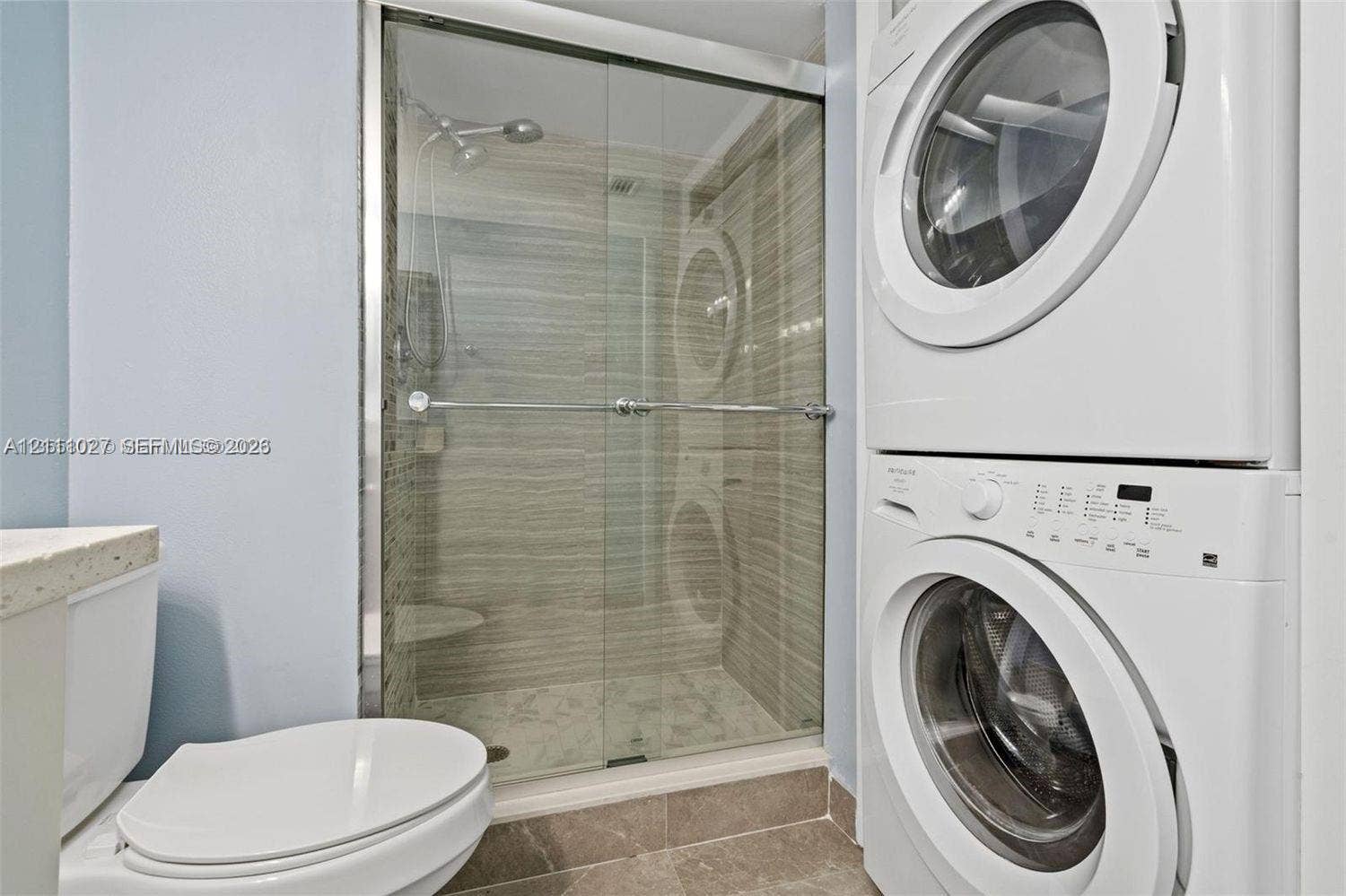 Shower with sliding glass enclosure and tiled walls, stacked washer and dryer unit, and ceramic floor tiling