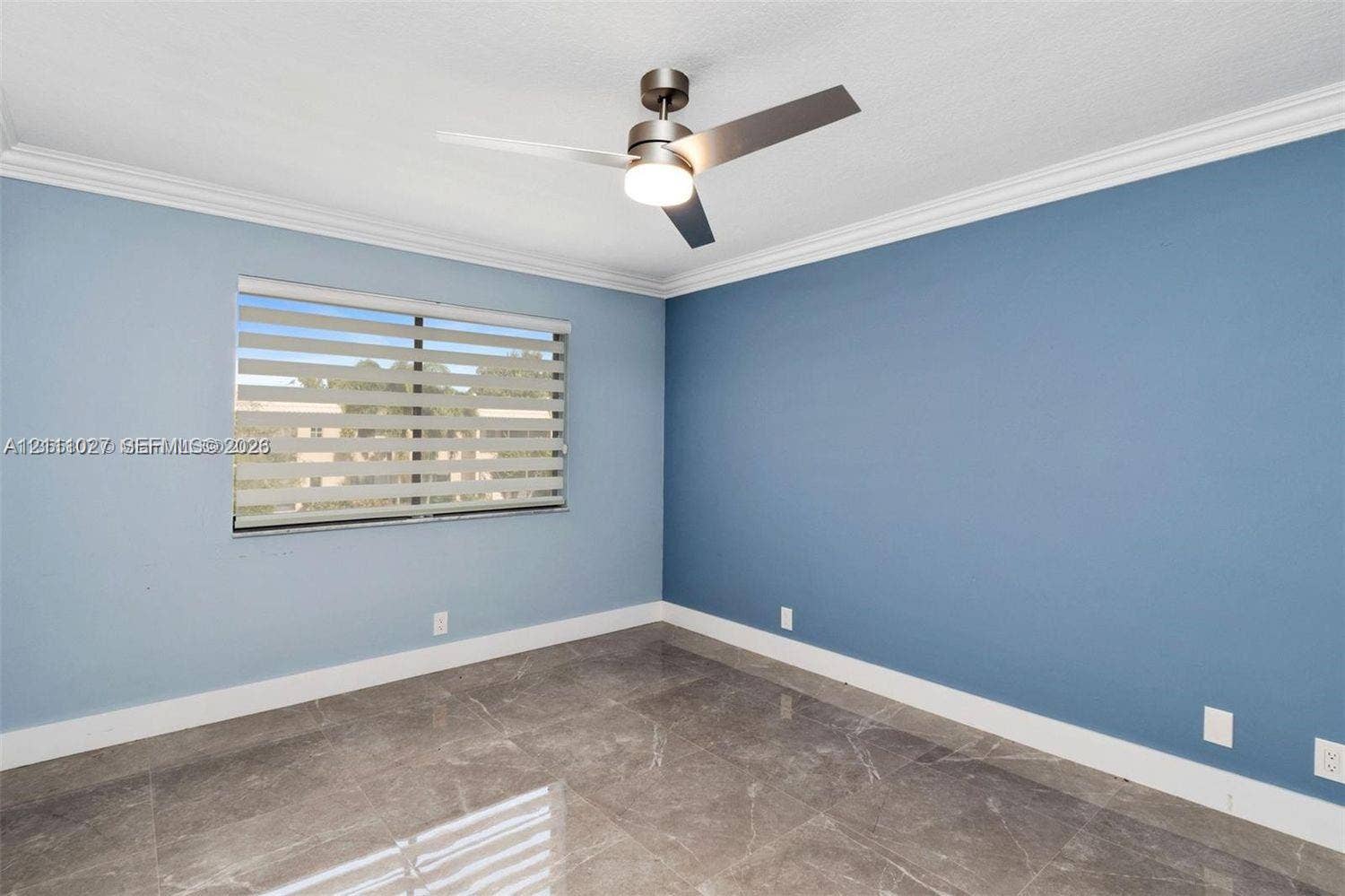 Room featuring large-format tile flooring, crown molding, a modern three-blade ceiling fan with integrated lighting, and dual-layered window shades