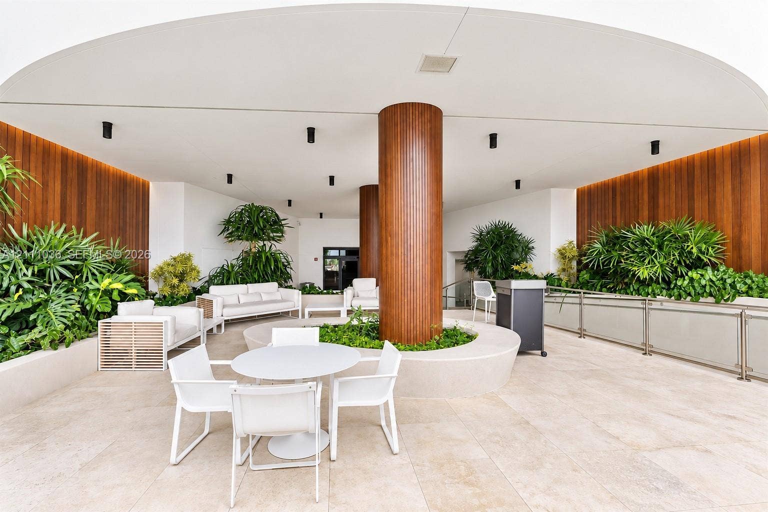6365 Collins Avenue, #3811, Miami Beach, FL 33141 Covered outdoor terrace featuring large-format stone tile flooring, warm wood-paneled walls, integrated recessed lighting, and a central structural column with a circular built-in planter