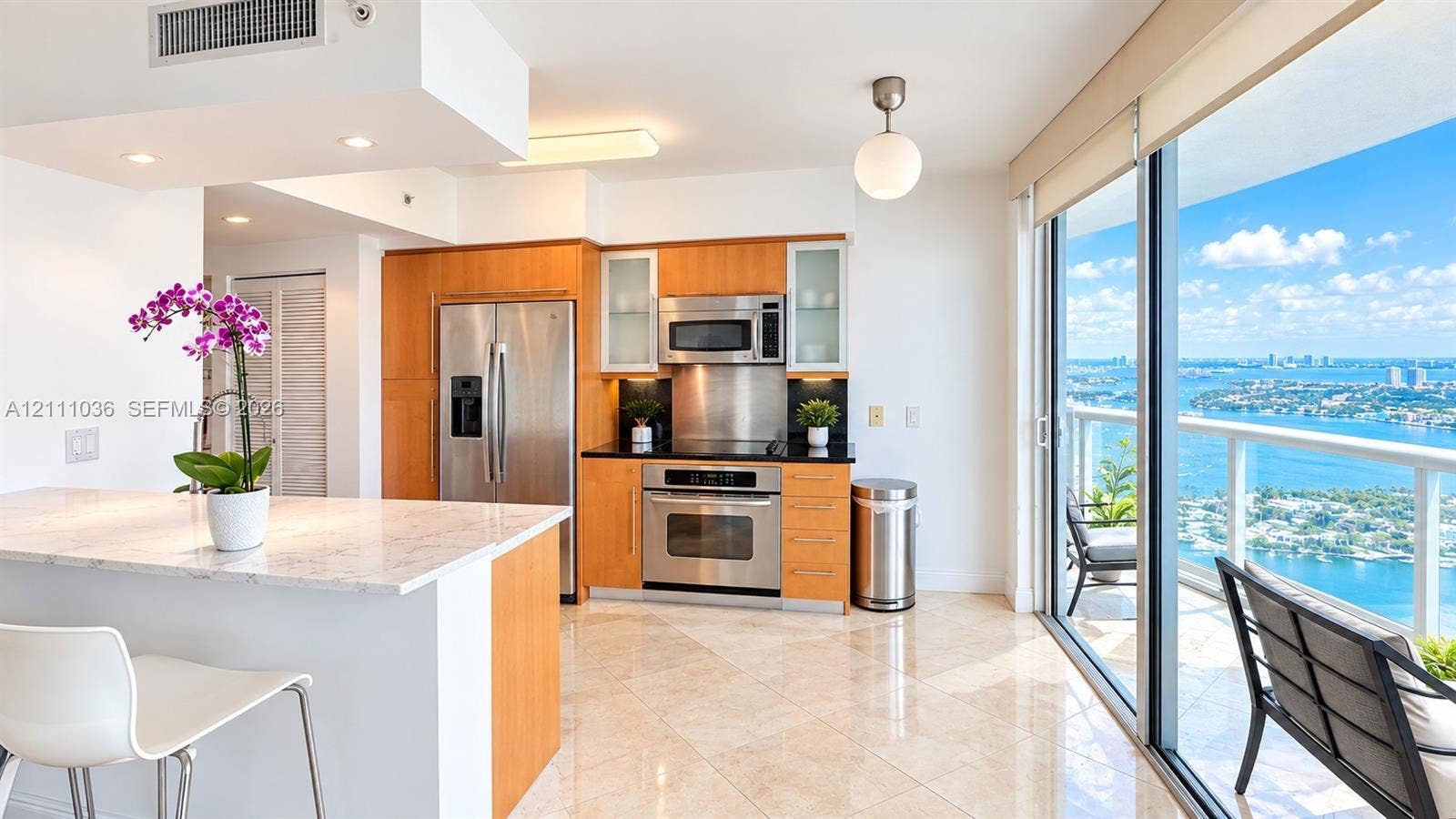 6365 Collins Avenue, #3811, Miami Beach, FL 33141 Kitchen featuring wood-finish cabinetry, stainless steel appliances, stone-topped island, polished tile flooring, and floor-to-ceiling glass sliding doors
