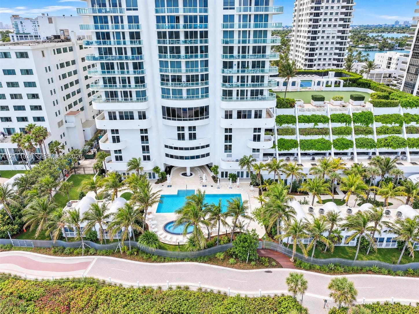 6365 Collins Avenue, #3811, Miami Beach, FL 33141 High-rise residential exterior featuring expansive glass balconies, a ground-level swimming pool, a separate spa, landscaped grounds with mature palm trees, and multi-level terraced gardens