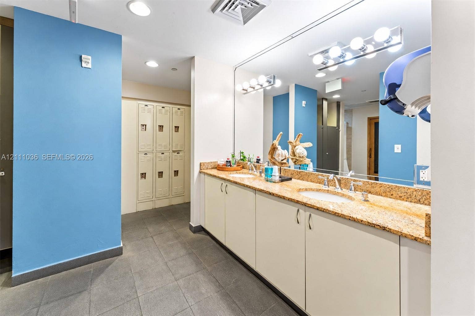 6365 Collins Avenue, #3811, Miami Beach, FL 33141 Dual-sink vanity with solid-surface countertop, floor-to-ceiling metal lockers, large-format tile flooring, and multi-bulb wall lighting