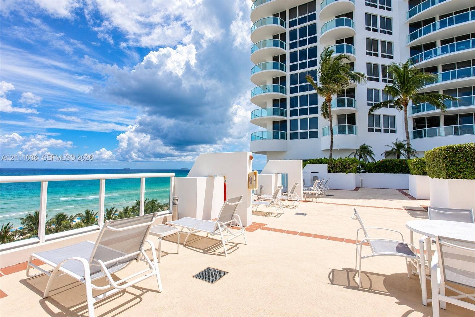 6365 Collins Avenue, #3811, Miami Beach, FL 33141 Expansive outdoor terrace featuring stone-finish flooring, glass-paneled railings, high-rise architectural facade, and manicured perimeter hedges