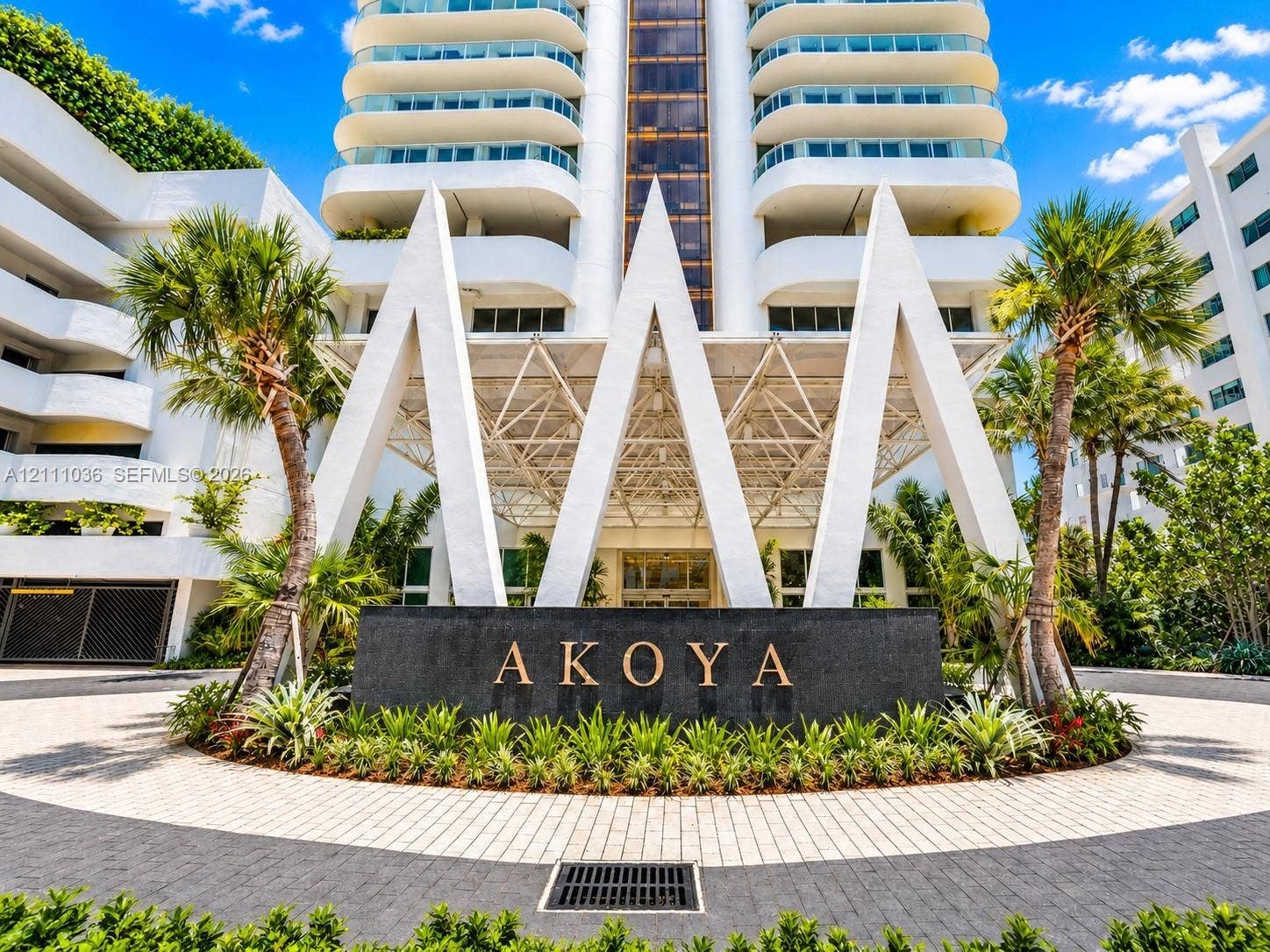 6365 Collins Avenue, #3811, Miami Beach, FL 33141 High-rise building featuring a geometric canopy entrance, stone-finished signage, curved balcony detailing, and a paver stone circular driveway