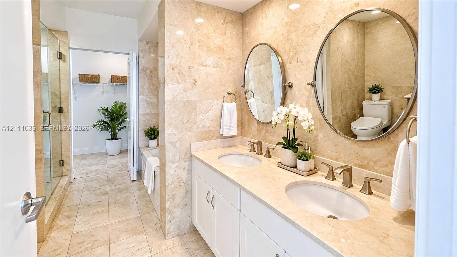 6365 Collins Avenue, #3811, Miami Beach, FL 33141 Double vanity featuring white cabinetry, stone-finish countertops, dual oval mirrors, and wall-mounted metallic fixtures, accented by floor-to-ceiling stone wall tiling and a glass-enclosed shower