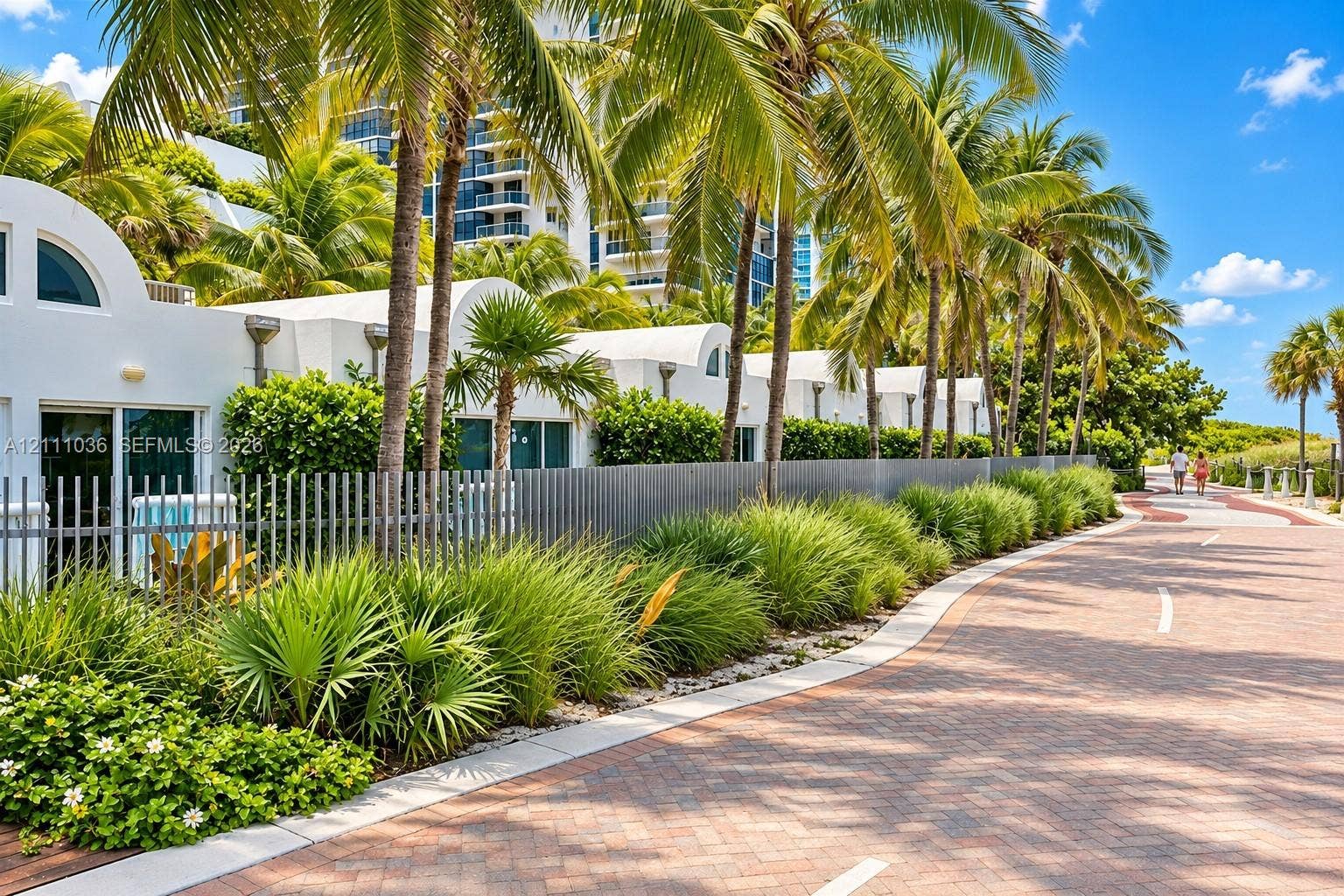 6365 Collins Avenue, #3811, Miami Beach, FL 33141 Stucco exterior featuring arched rooflines, integrated metal fencing, mature palm trees, and native ornamental landscaping situated along a paved brick path