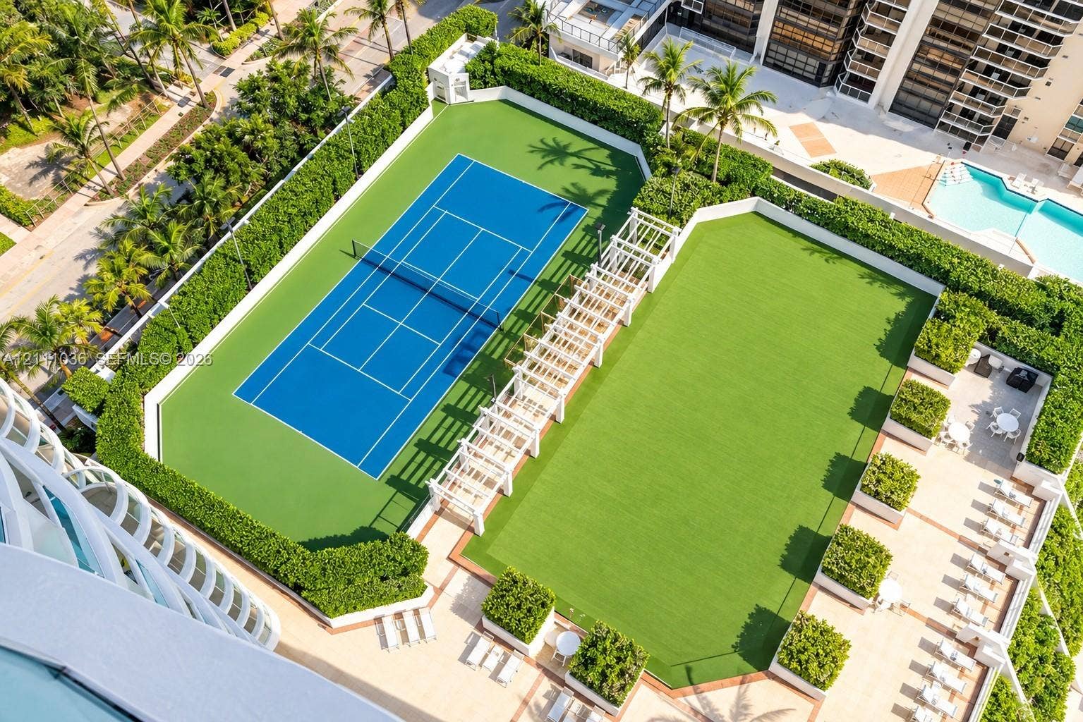 6365 Collins Avenue, #3811, Miami Beach, FL 33141 Tennis court, expansive synthetic turf lawn, white pergola structure, and landscaped privacy hedging
