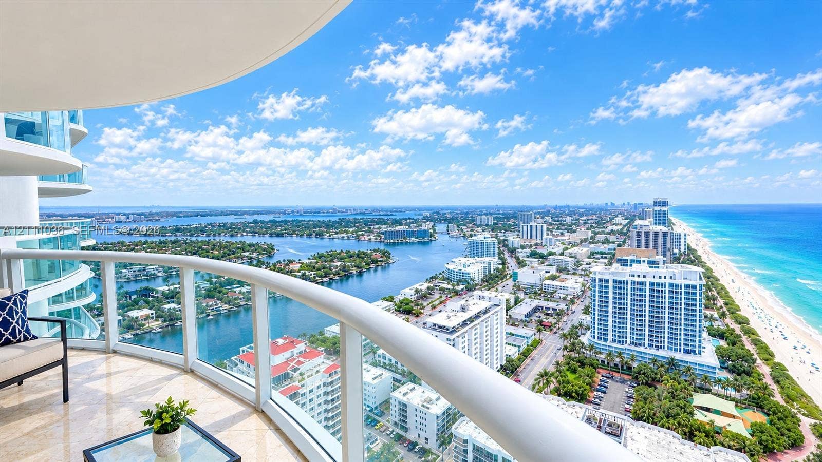 6365 Collins Avenue, #3811, Miami Beach, FL 33141 Curved covered balcony featuring stone flooring and glass-panel railings with expansive coastal and cityscape scenery