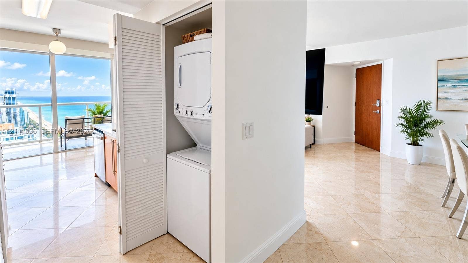 6365 Collins Avenue, #3811, Miami Beach, FL 33141 In-unit laundry closet featuring white louvered folding doors, floor-to-ceiling glass paneling, tile flooring, and a solid-core wood entry door