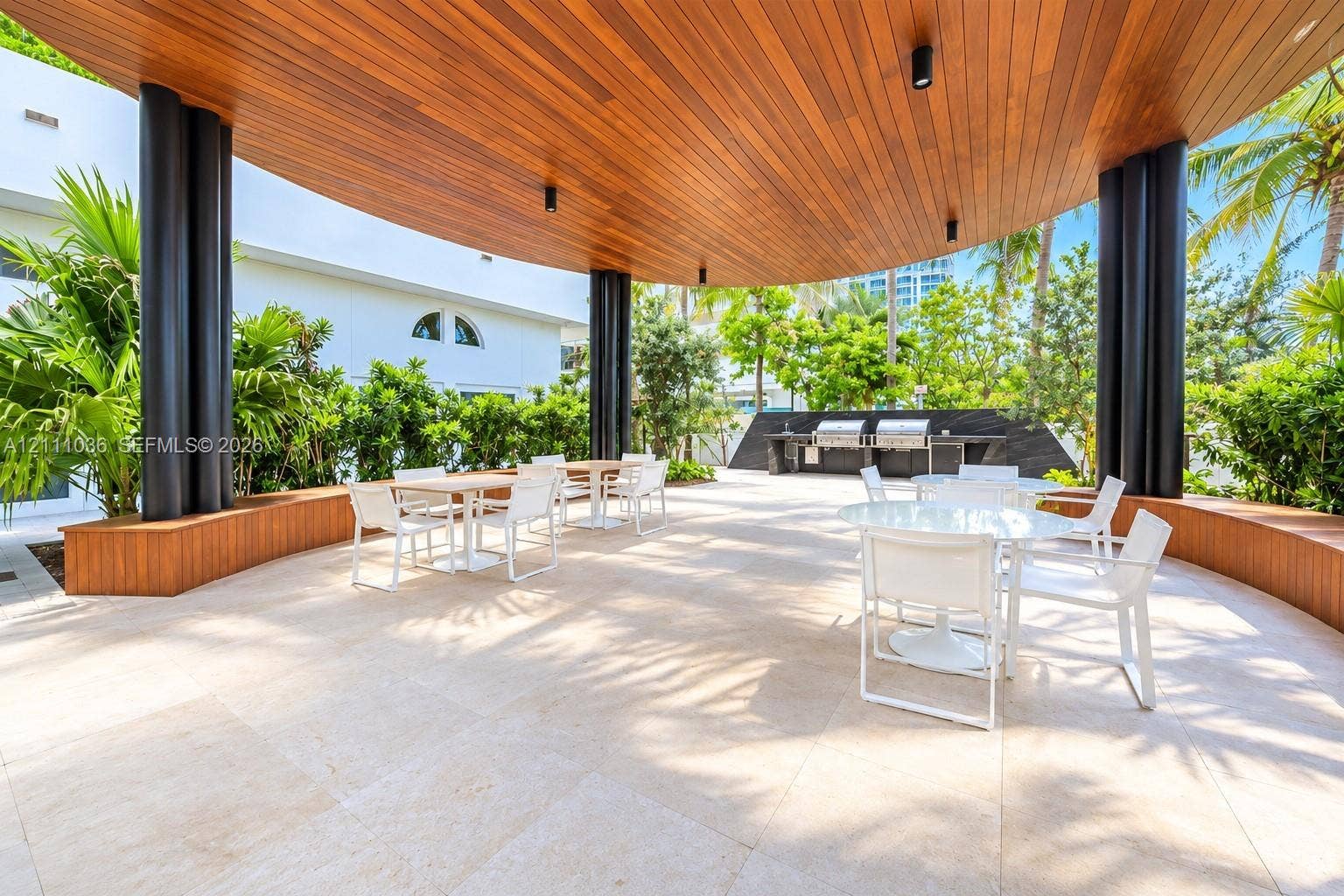 6365 Collins Avenue, #3811, Miami Beach, FL 33141 Covered outdoor terrace featuring a wood-paneled ceiling, stone tile flooring, structural cylindrical columns, and a built-in outdoor kitchen station with stainless steel grills
