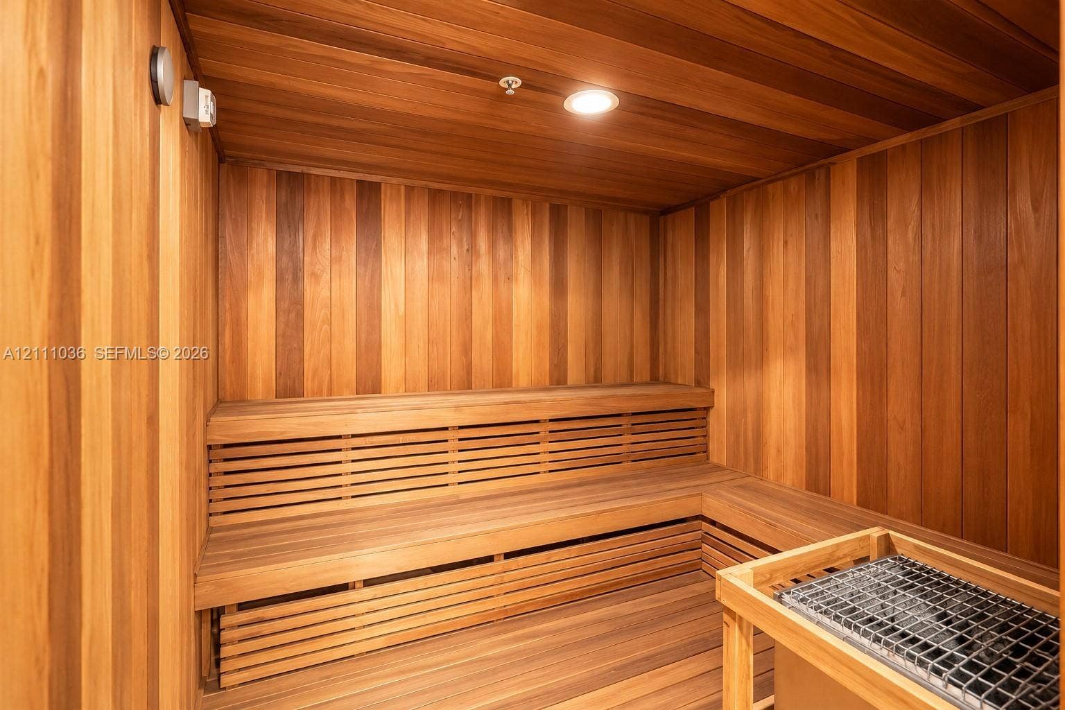 6365 Collins Avenue, #3811, Miami Beach, FL 33141 Sauna featuring tongue-and-groove wood paneling, multi-level built-in bench seating, recessed ceiling lighting, and a stone-filled heating unit with a wooden safety enclosure