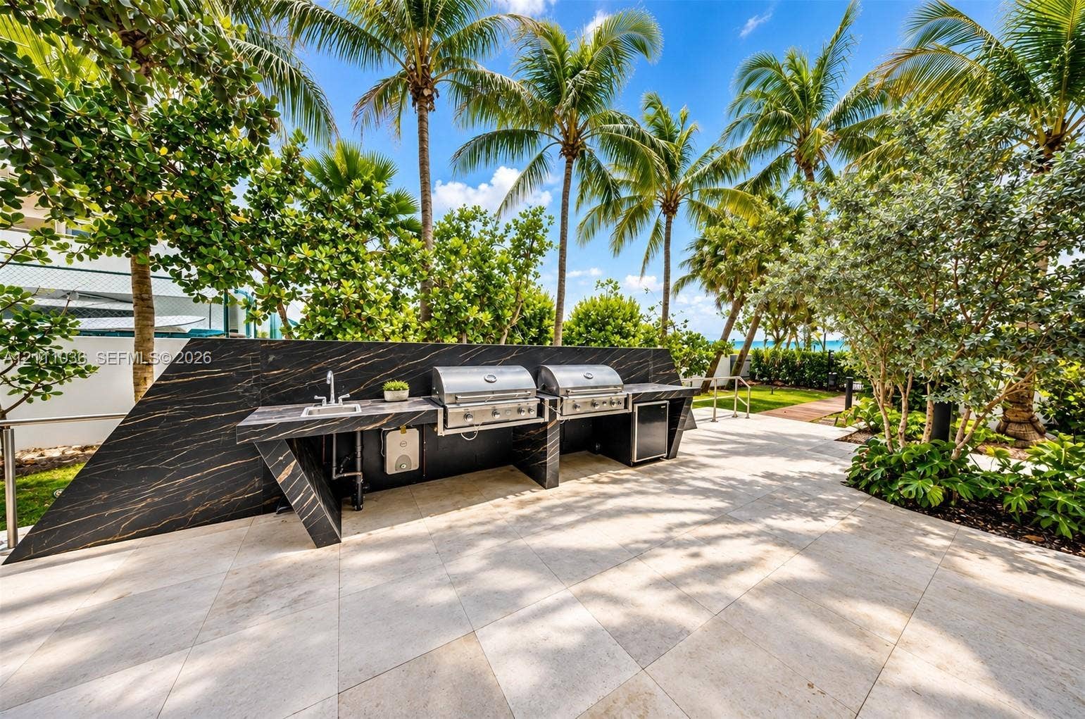 6365 Collins Avenue, #3811, Miami Beach, FL 33141 Outdoor kitchen featuring a sleek, dark-veined stone countertop, built-in stainless steel dual grills, an integrated stainless steel sink, and light-toned tile flooring