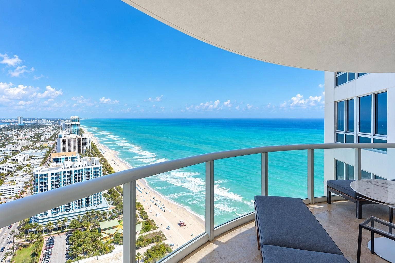 6365 Collins Avenue, #3811, Miami Beach, FL 33141 Curved covered balcony with stone flooring and glass panel railing overlooking the coastline