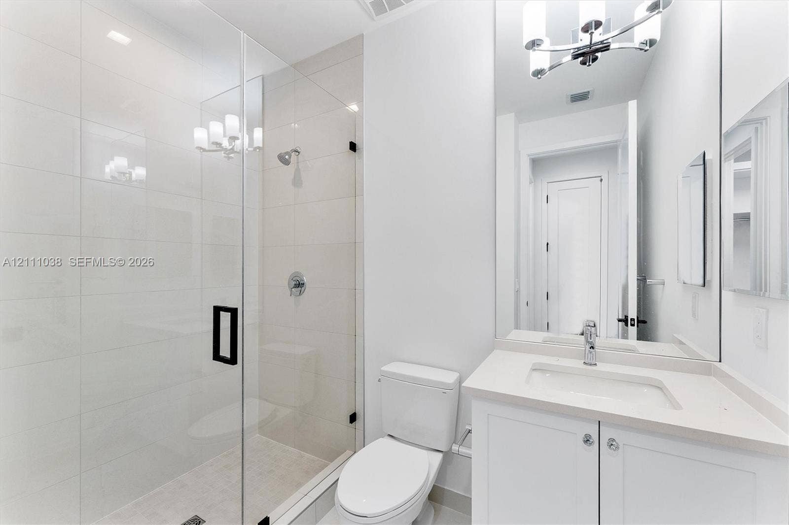 Walk-in shower with floor-to-ceiling tile, frameless glass enclosure, and matte black hardware, paired with a white vanity featuring a stone-composite countertop and an expansive wall-mounted mirror