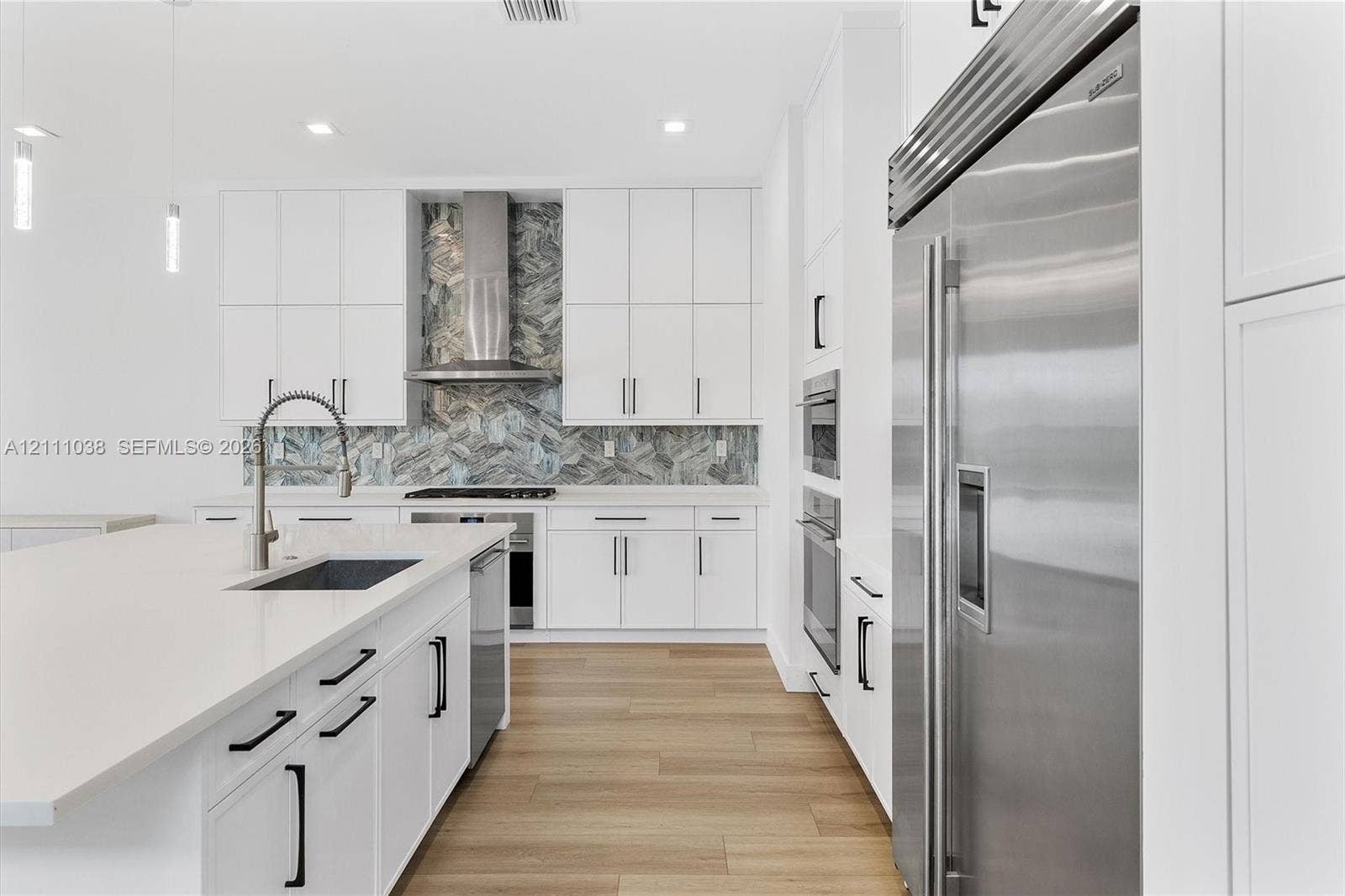 Kitchen featuring white cabinetry, wood-finish flooring, a herringbone-patterned stone backsplash, stainless steel appliances, and a quartz-topped center island