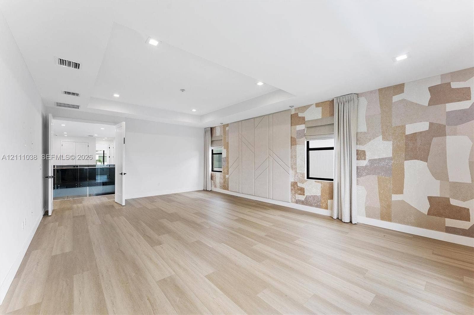Tray ceiling with recessed lighting, wood-finish flooring, custom geometric wall paneling, and neutral-toned patterned wall covering