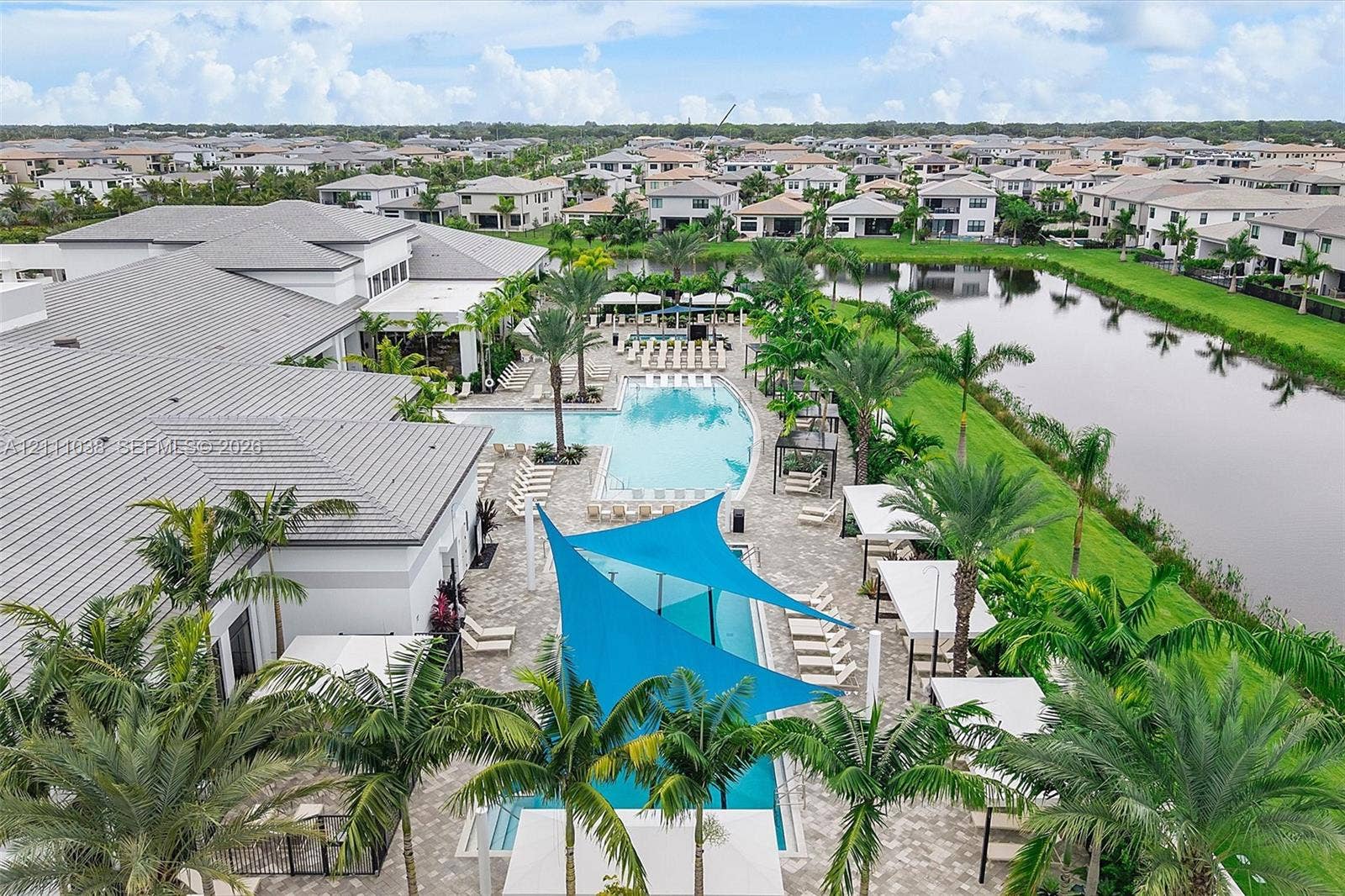 Resort-style swimming pool, expansive paver patio, integrated shade structures, tropical landscaping, and waterfront scenery