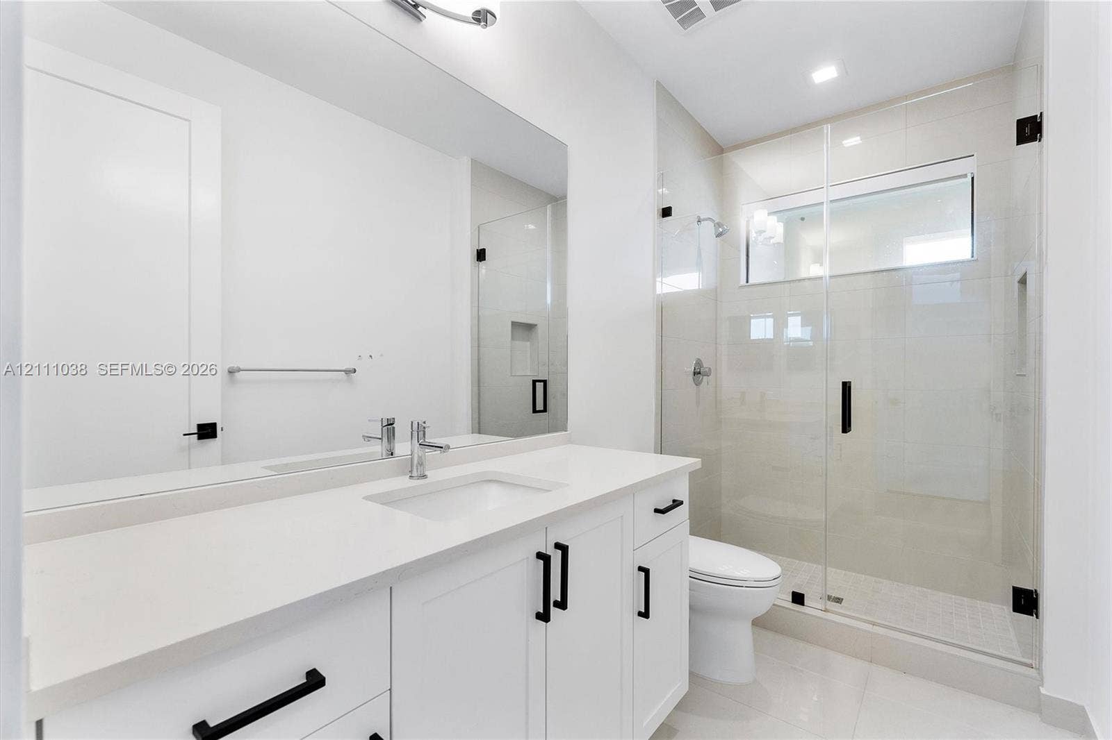 White cabinetry vanity with solid surface countertop, glass-enclosed shower with tiled walls and built-in niche, and matte black hardware fixtures