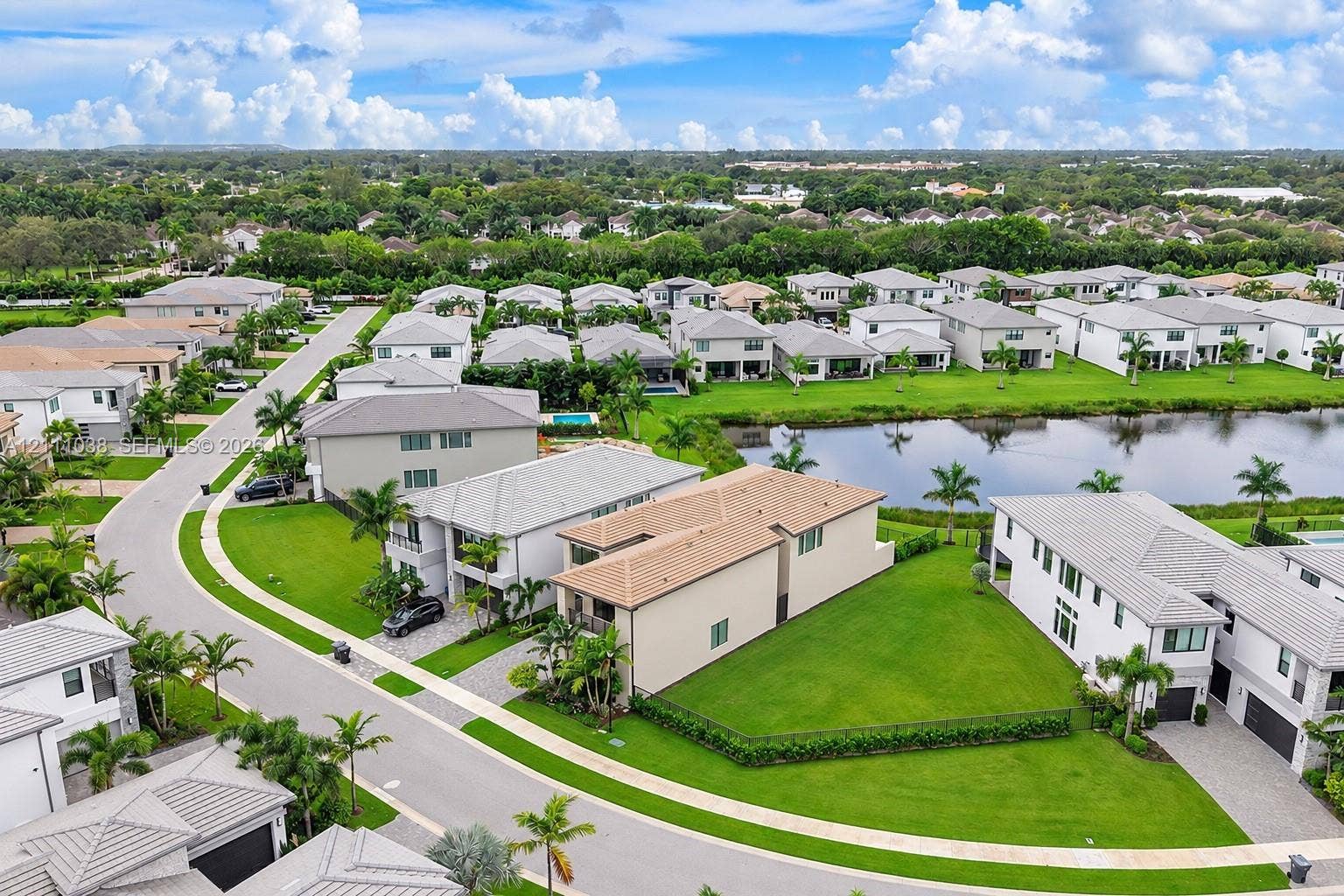 Aerial perspective of a multi-story residence featuring a concrete tile roof, paver driveway, expansive side lawn, and direct proximity to a central water feature