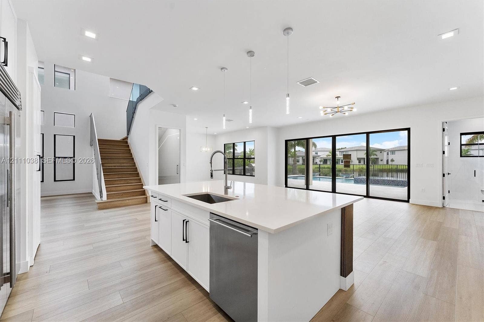 Open-concept kitchen featuring a center island with a quartz countertop, stainless steel dishwasher, and under-mount sink, complemented by wood-finish flooring, recessed lighting, and multi-panel sliding glass doors