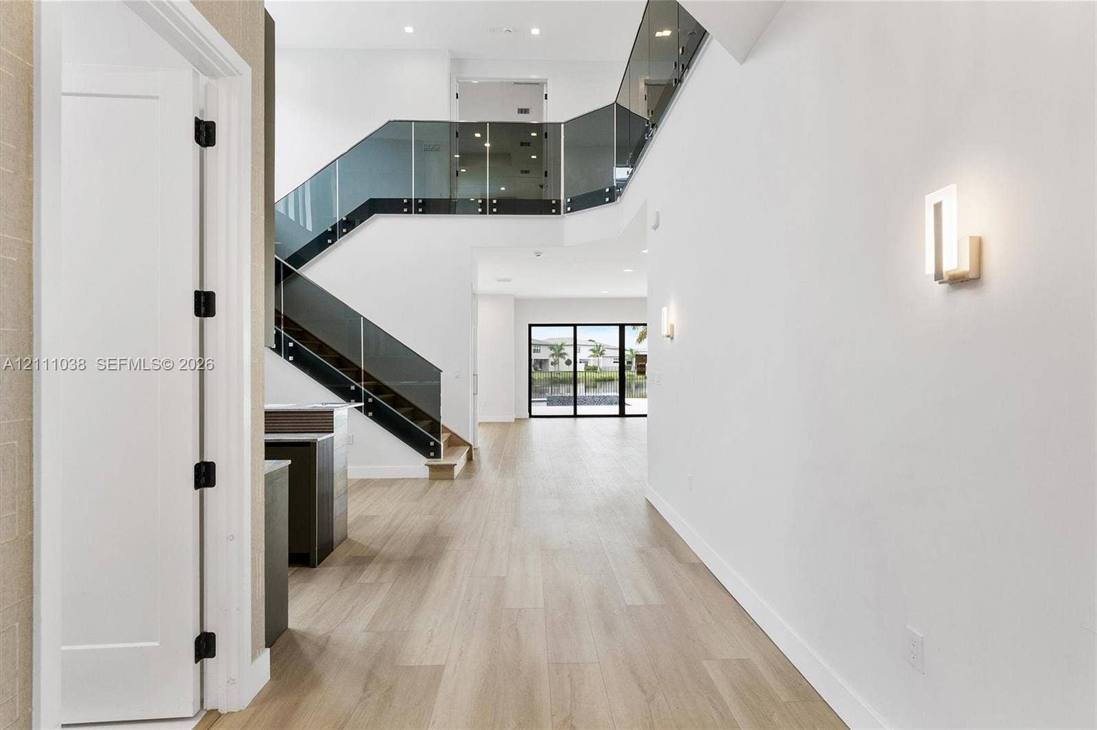 Two-story foyer featuring wood-finish flooring, a glass-paneled staircase with metal hardware, recessed lighting, and modern wall-mounted light fixtures
