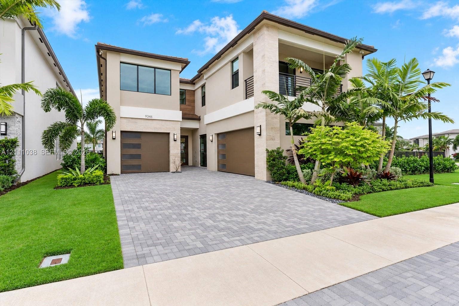 Two-story contemporary exterior featuring stone facade accents, a multi-car garage, upper-level covered balcony, and custom-paver driveway