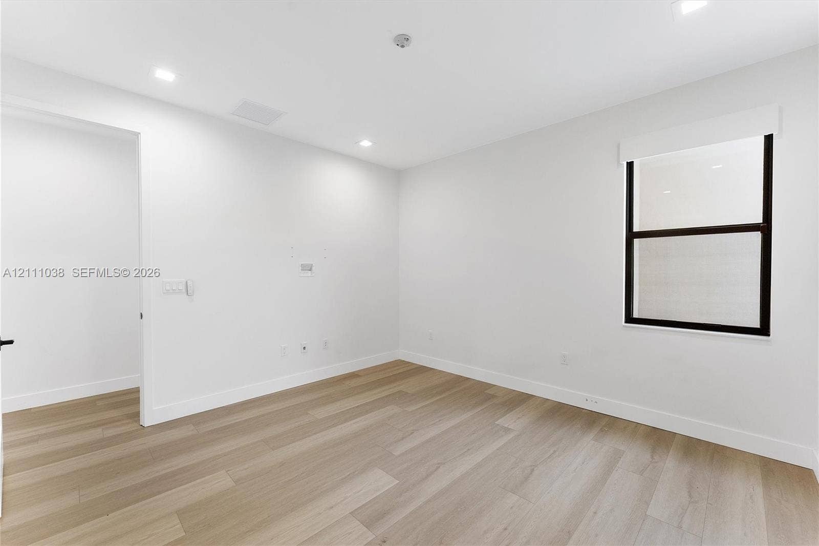 Neutral interior featuring wood-finish flooring, recessed lighting, and a window with a dark-finished frame