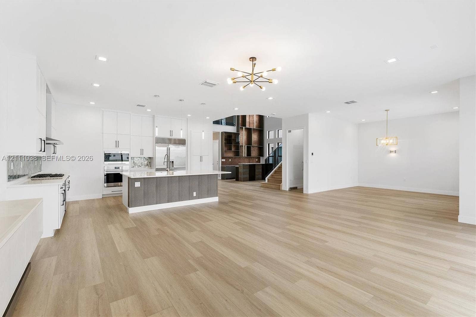 Open-concept area featuring wood-finish flooring, a kitchen island with stone countertop, white cabinetry with contrast base, modern chandelier lighting, and recessed ceiling lights