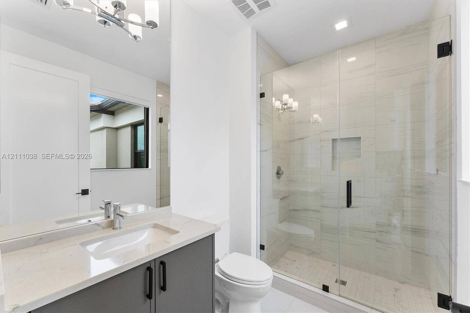 Bathroom featuring a vanity with stone-finish countertop, undermount sink, frameless glass-enclosed shower with floor-to-ceiling tile, and matte black hardware