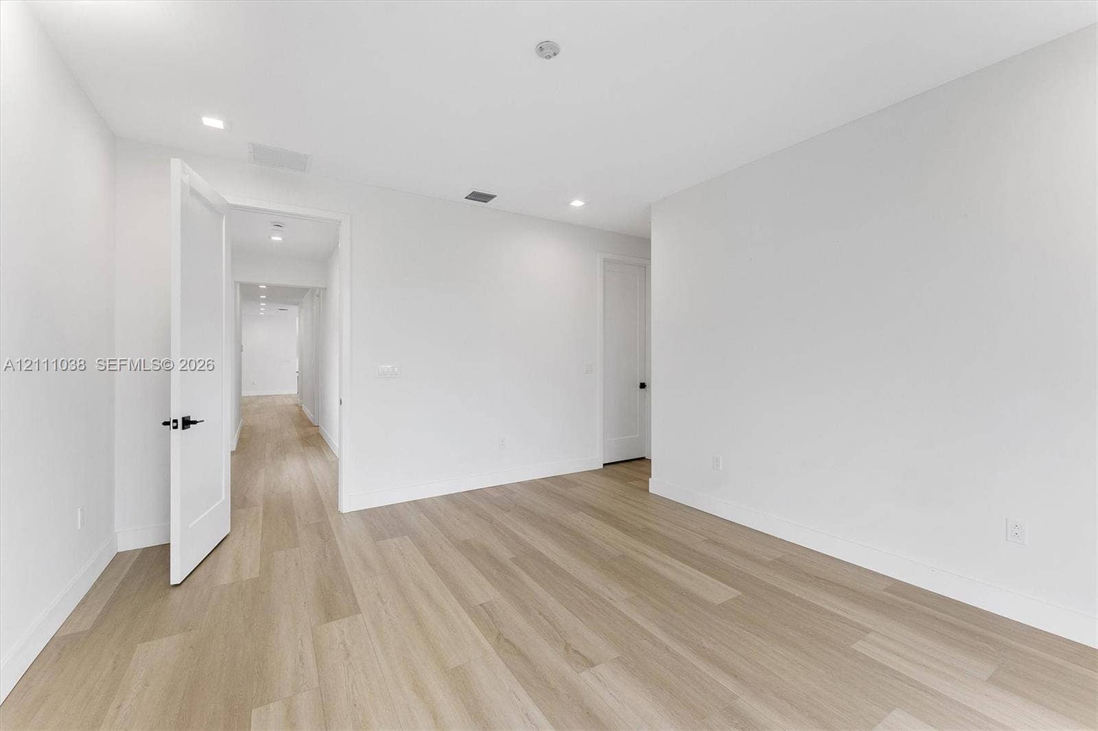 Neutral interior space featuring wood-finish flooring, recessed lighting, and solid-core doors with matte black hardware