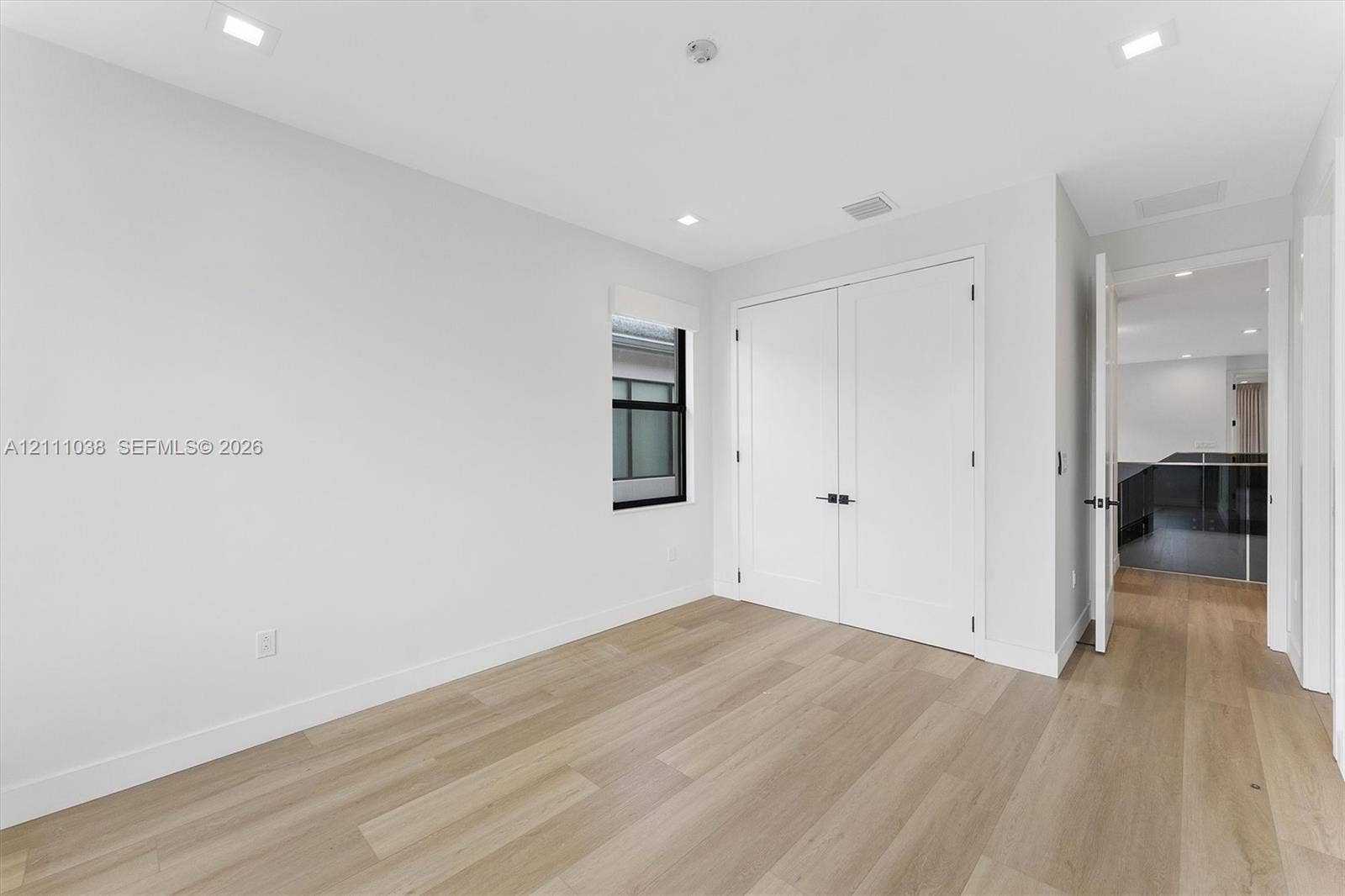 Neutral-toned interior featuring wood-finish flooring, recessed lighting, white double closet doors with matte black hardware, and a window with a black frame