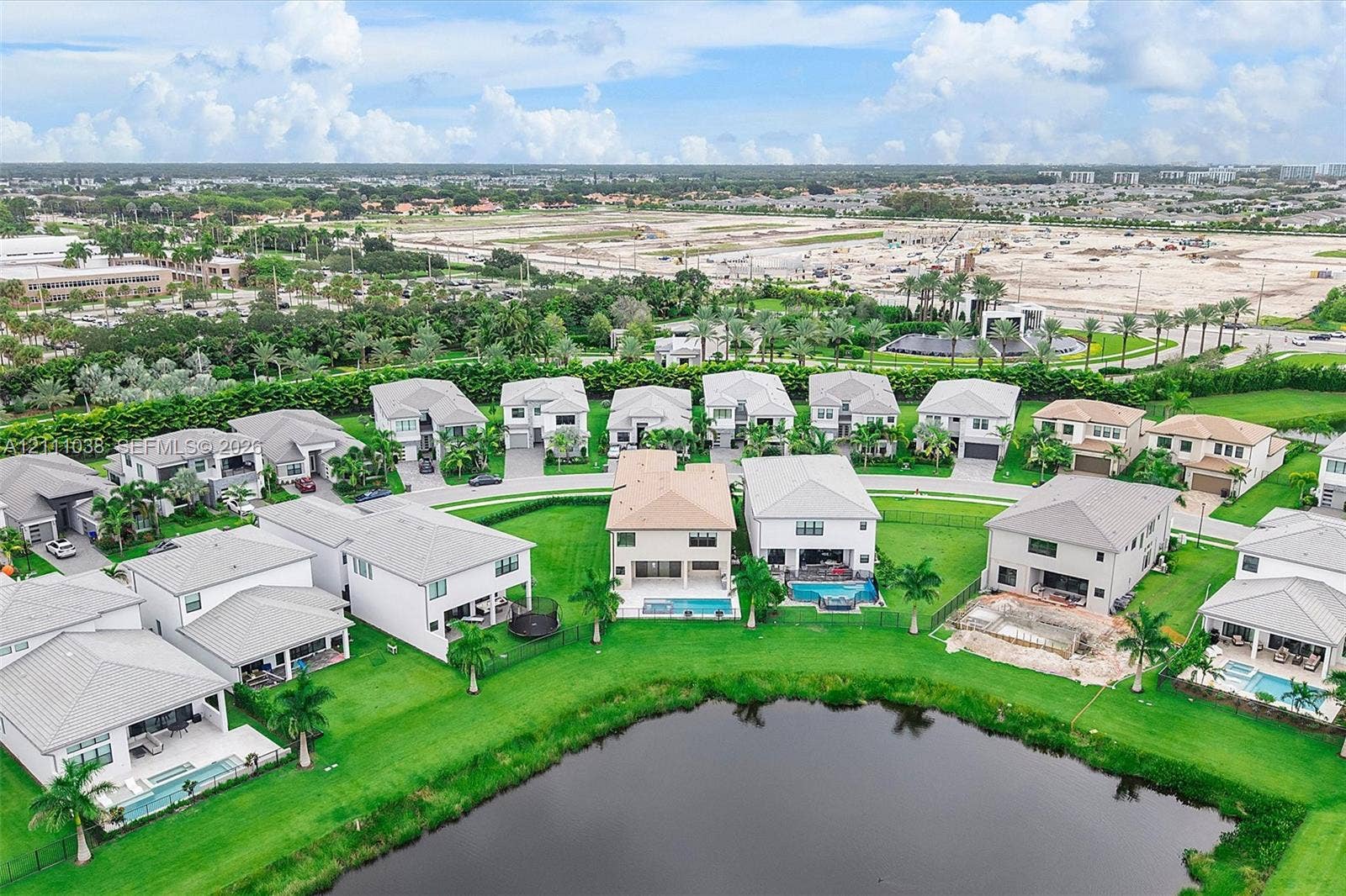 Aerial perspective of a residential community featuring multi-story dwellings, manicured lawns, palm tree landscaping, and a central water feature